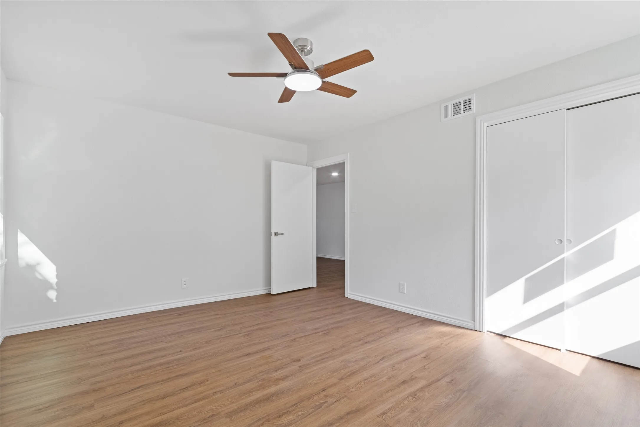 Spacious room featuring wood-finish flooring, white walls, and a ceiling fan with light fixture