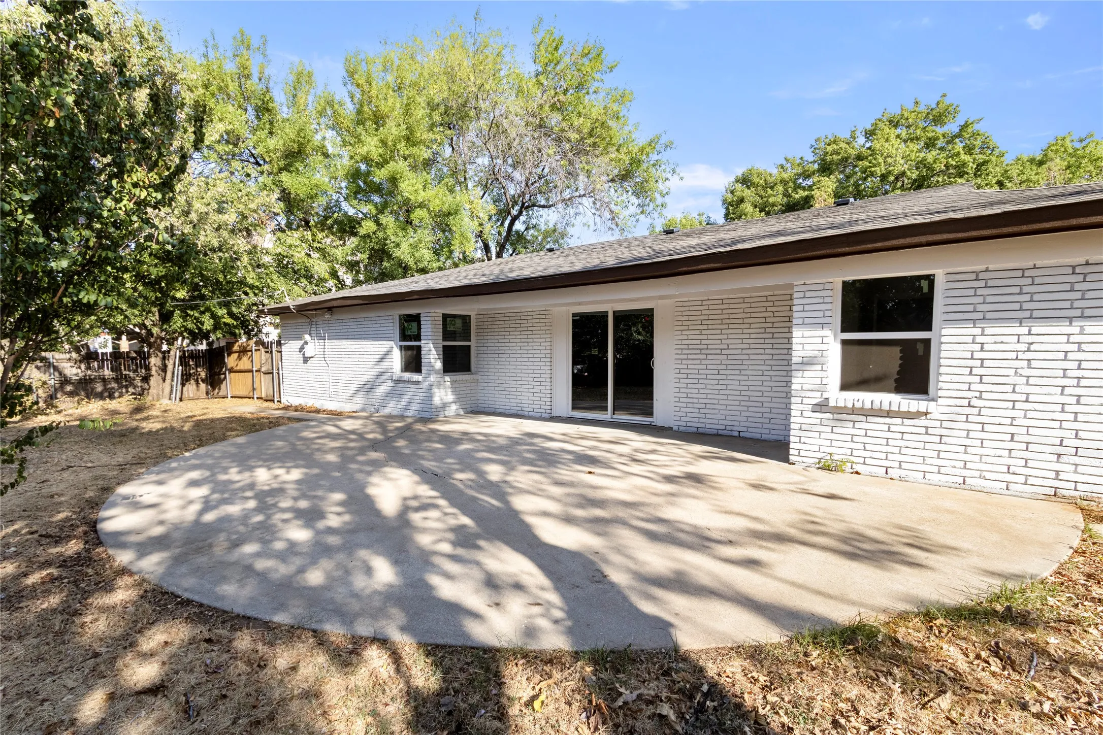 White brick exterior with a large circular concrete patio, sliding glass door, and multiple windows