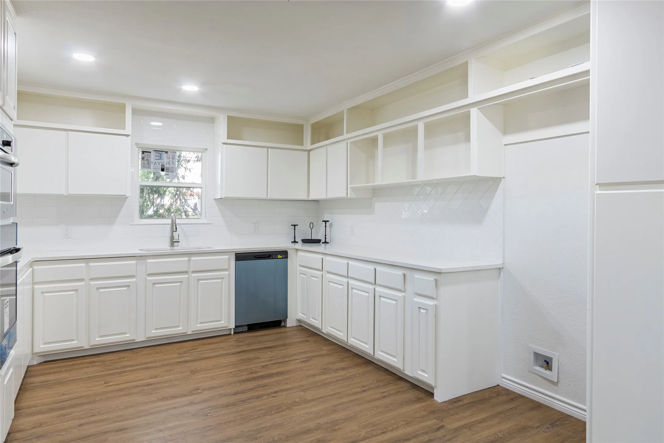 Kitchen featuring white cabinetry, white countertops, a mosaic tile backsplash, a stainless steel sink, and wood-finish flooring