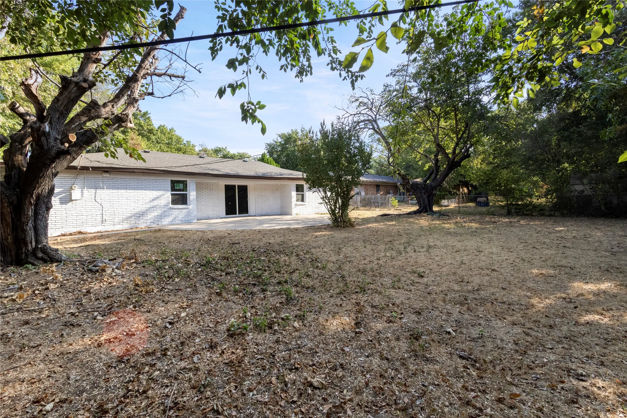 Expansive rear yard with mature trees, a durable brick exterior, a concrete patio, and sliding glass doors