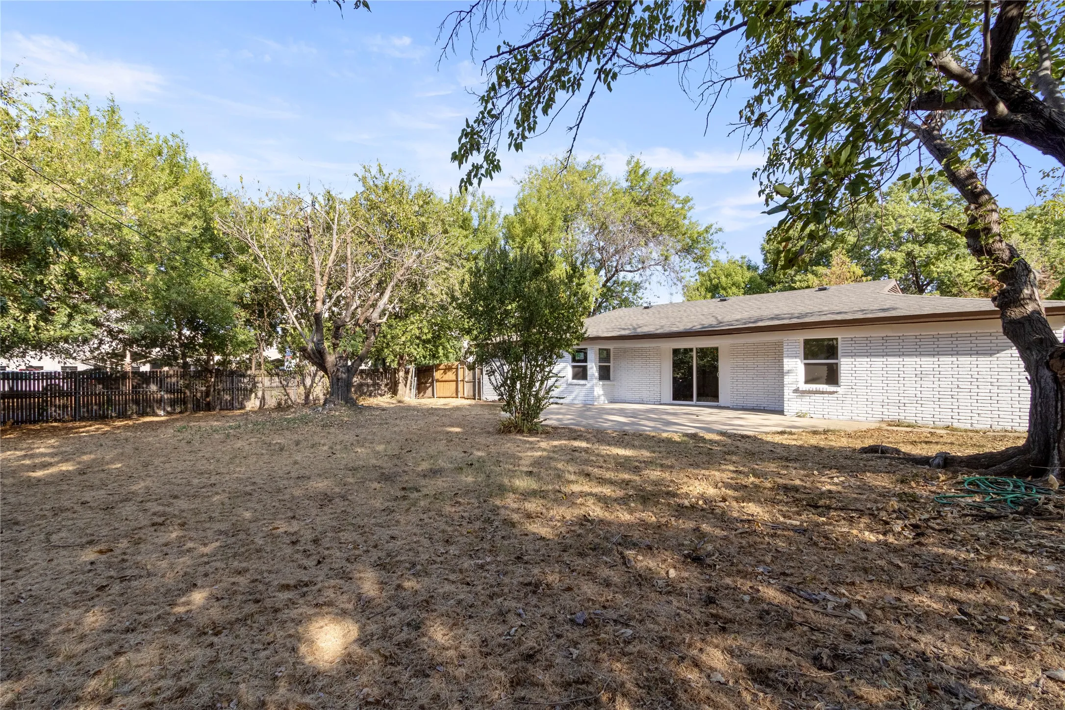 Expansive exterior featuring mature trees, a privacy fence, a brick facade, and a concrete patio