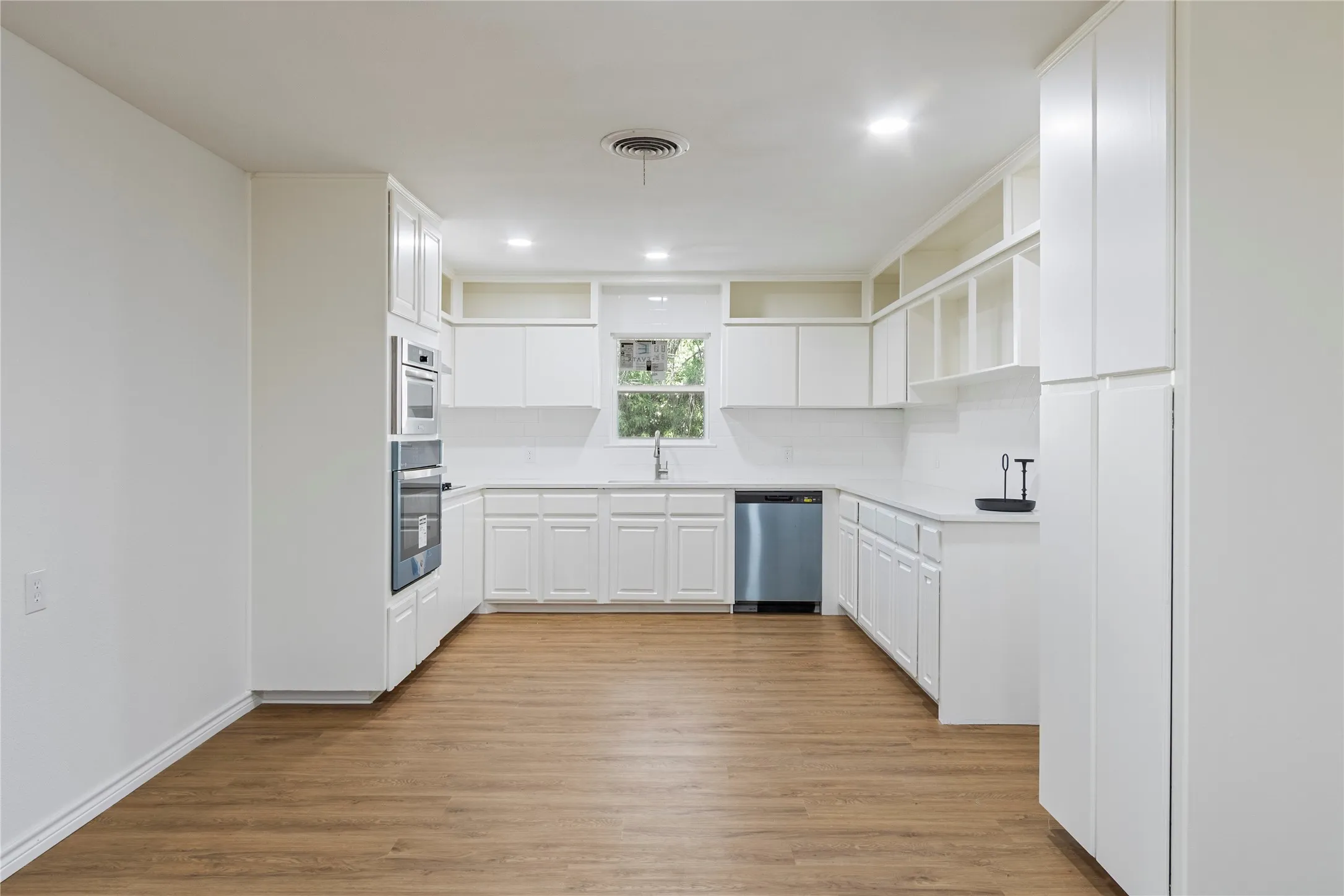 Kitchen featuring extensive white cabinetry, integrated stainless steel double ovens, wood-finish flooring, a stainless steel dishwasher, and recessed lighting