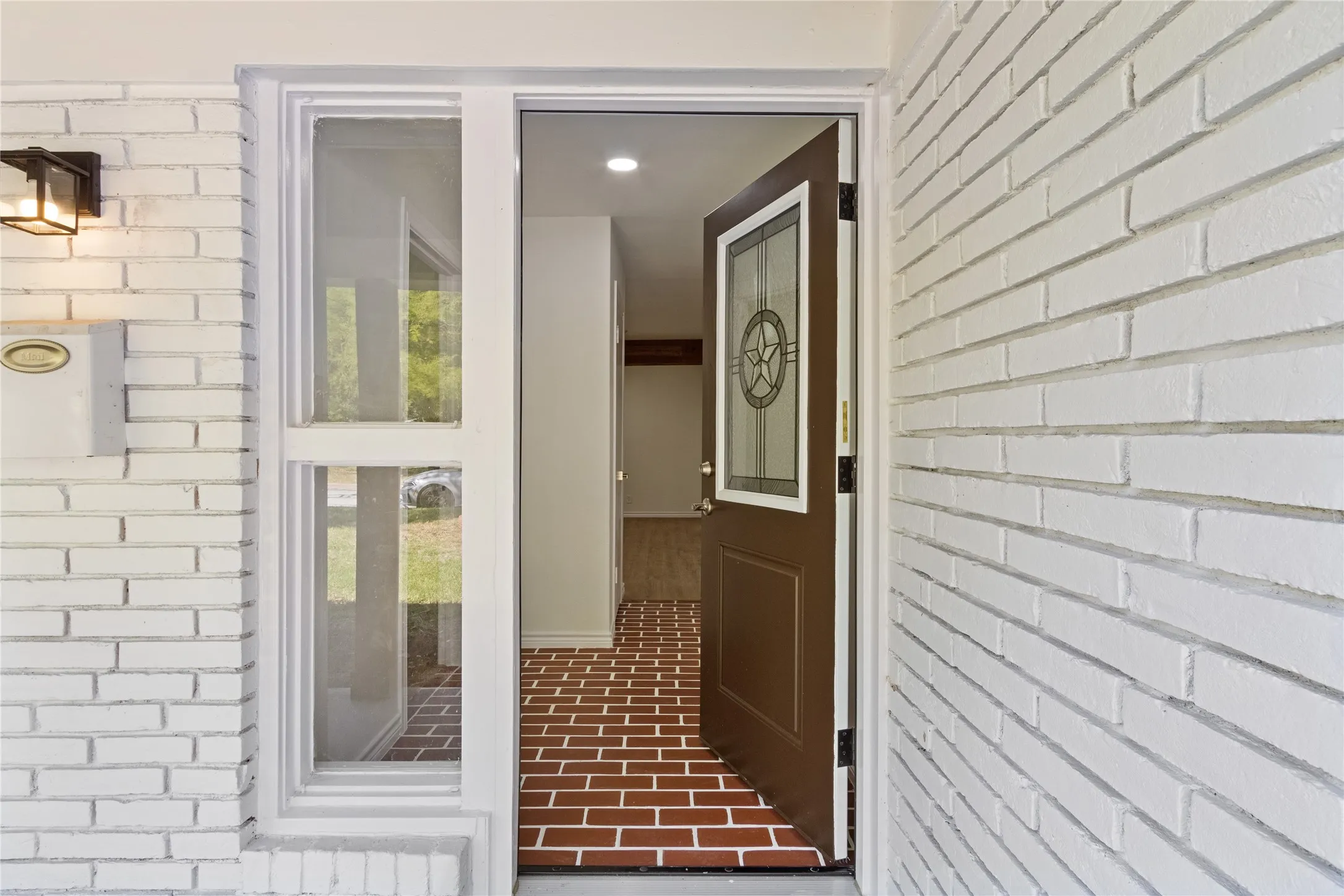 Exterior entryway featuring white painted brick, an open brown front door with decorative glass, and a sidelite window