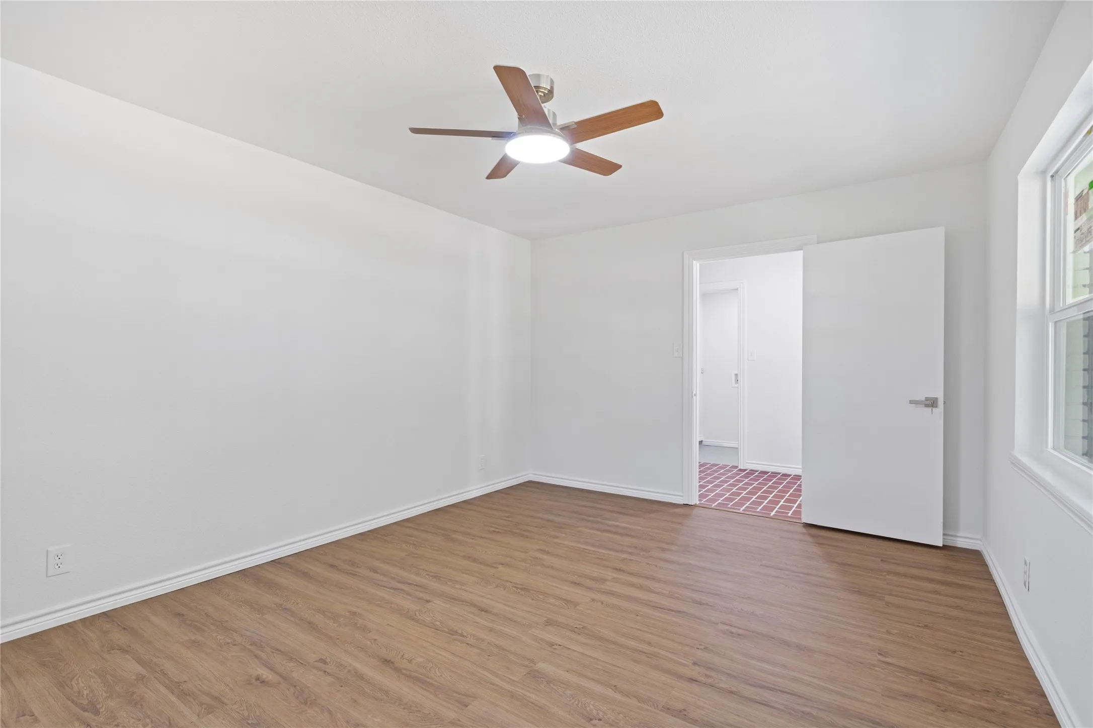 Room featuring wood-finish flooring, a ceiling fan with integrated lighting, and white baseboards
