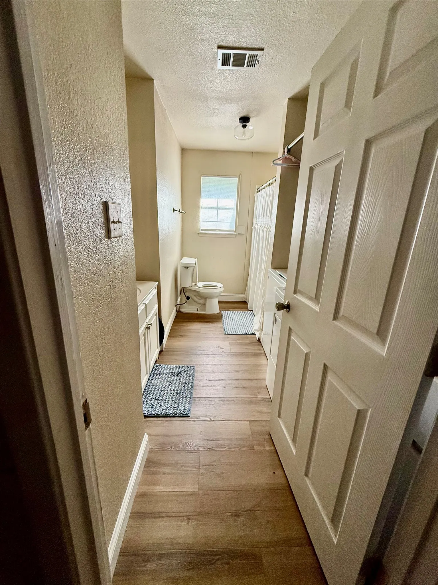 Bathroom featuring wood-finish flooring, a single window, white vanity, and a shower with a privacy curtain