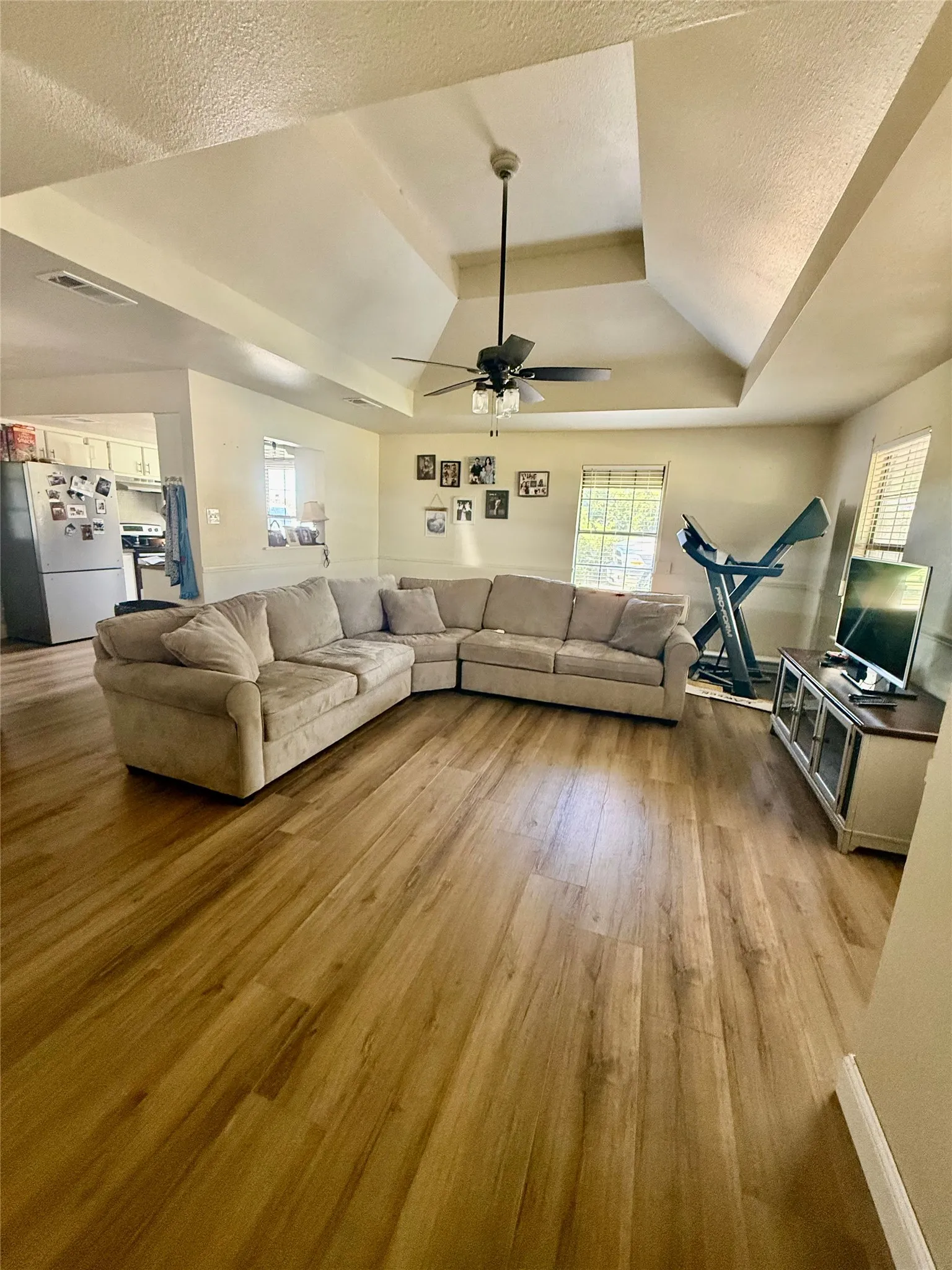 Spacious living area featuring wood-finish flooring, a tray ceiling, and a ceiling fan with integrated​​‌​​​​‌​​‌‌​‌‌​​​‌‌​‌​‌​‌​​​‌​​ lighting