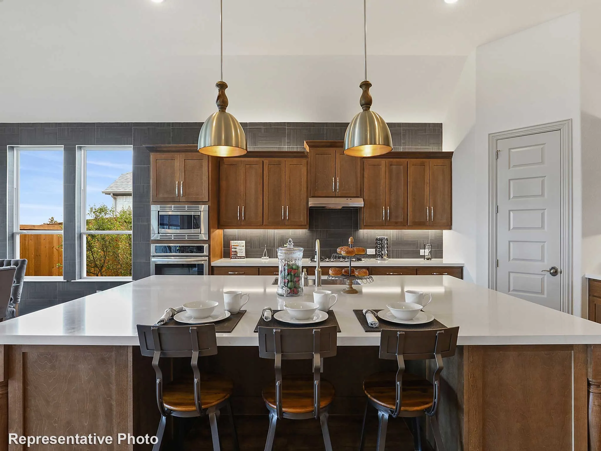 Expansive kitchen island with a light-toned countertop, rich wood-finish cabinetry, stainless steel built-in appliances, a tiled backsplash, and recessed lighting