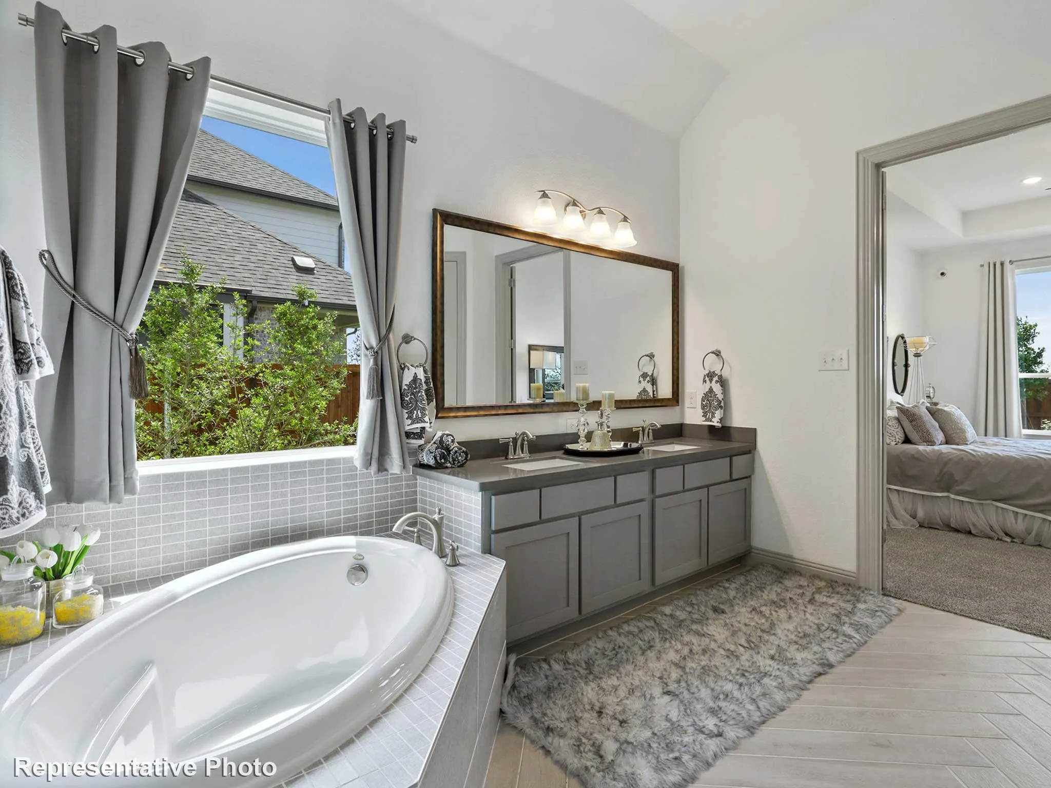 Bathroom featuring a built-in soaking tub with surrounding tile, a dual vanity with undermount sinks, a large framed mirror, and wood-finish flooring in a herringbone pattern