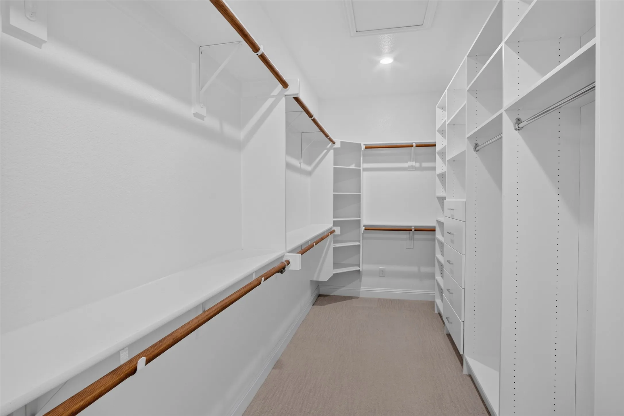 Expansive walk-in closet featuring white built-in shelving, multiple hanging rods, integrated drawers, and recessed ceiling lighting