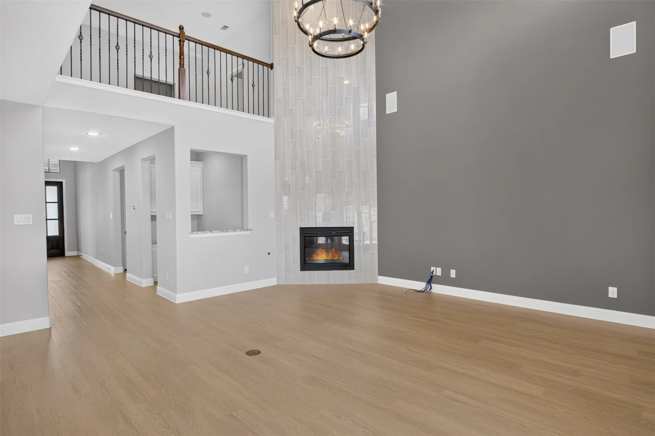 Spacious living area featuring high ceilings, wood-finish flooring, a contemporary fireplace with a tiled surround, a large chandelier, and an upper-level balcony with an iron railing