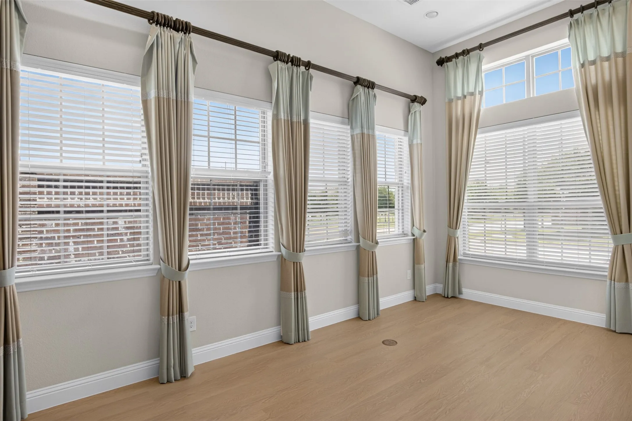 Spacious room featuring multiple large windows with horizontal blinds, wood-finish flooring, and light-colored walls