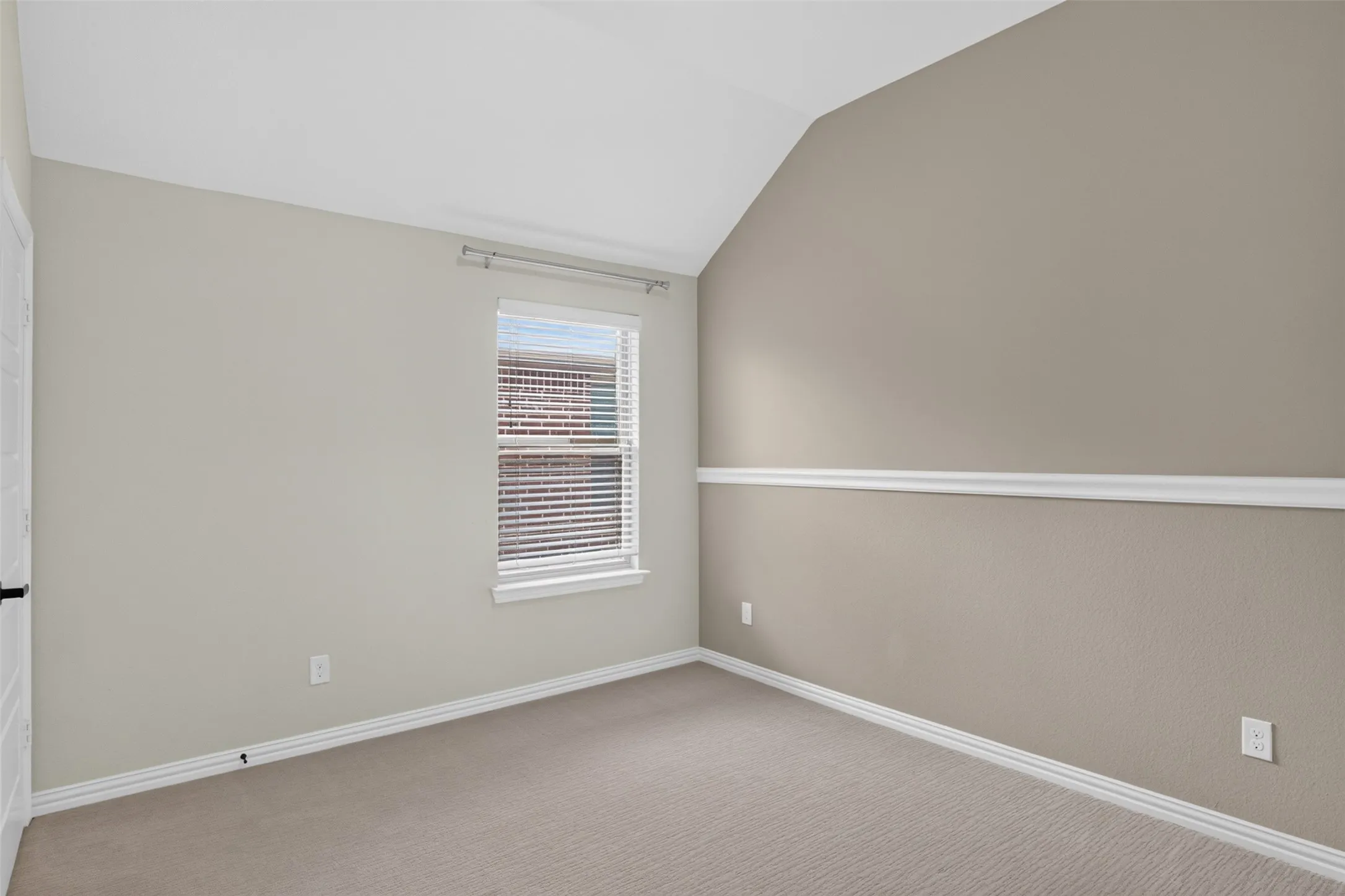 Carpeted room featuring a single window with blinds, vaulted ceiling, and chair rail molding