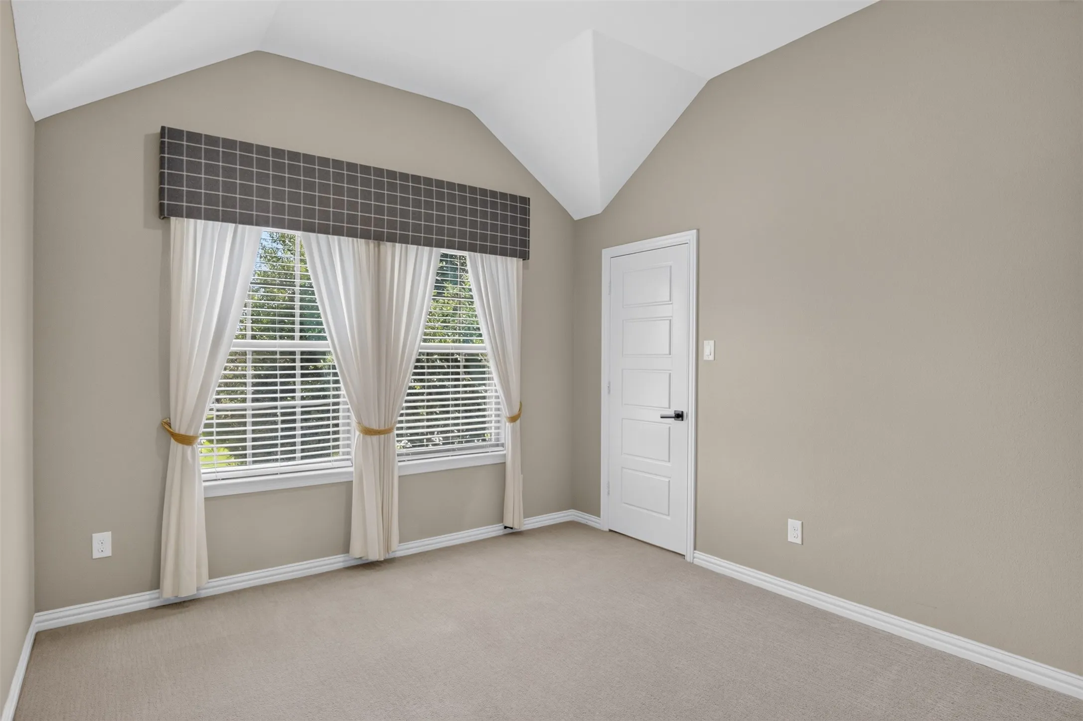 Vaulted ceiling room with neutral-toned walls and carpet flooring