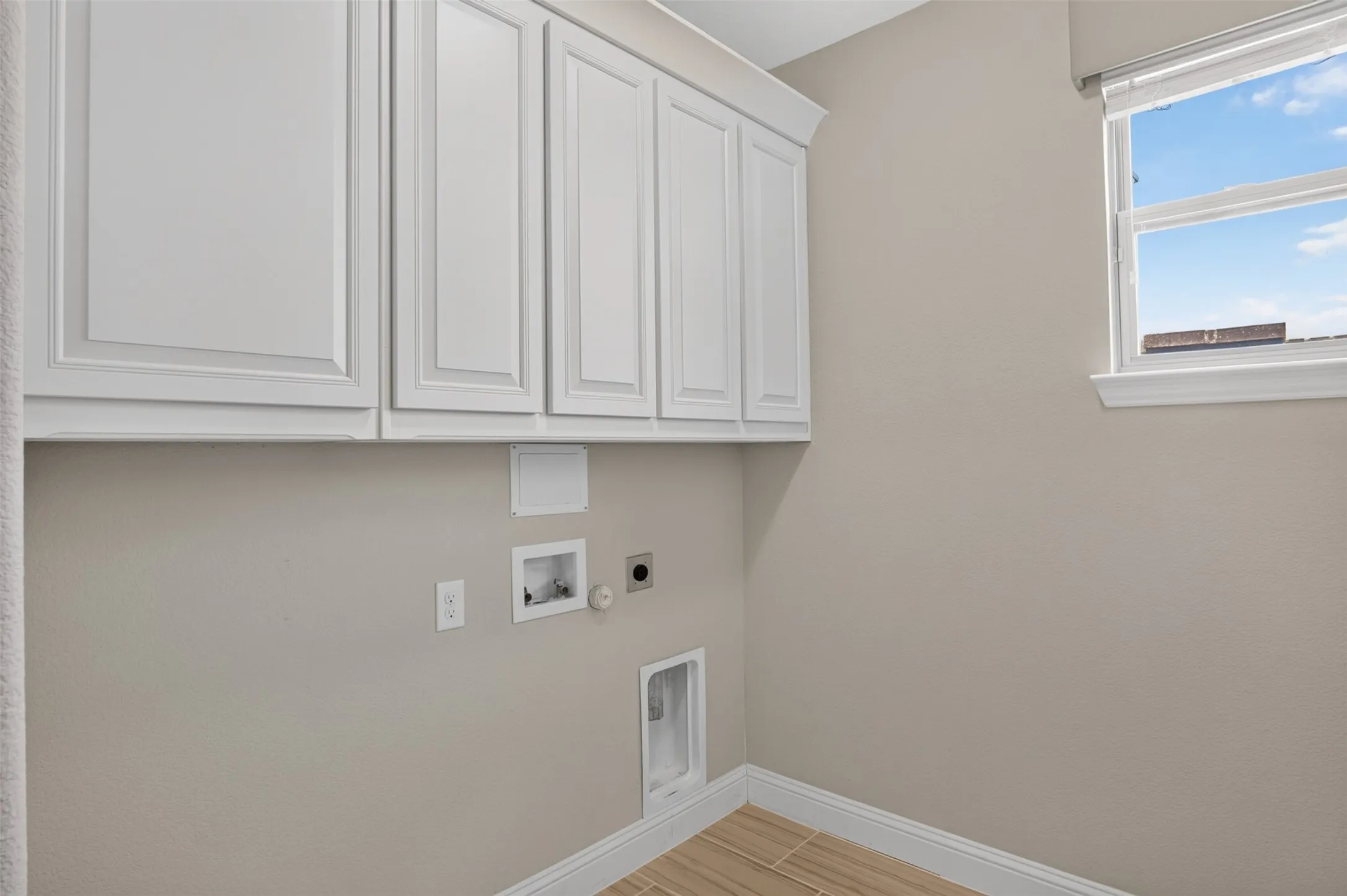 Laundry area featuring white shaker-style cabinetry, a window with natural light, neutral wall tones, and wood-finish tile flooring