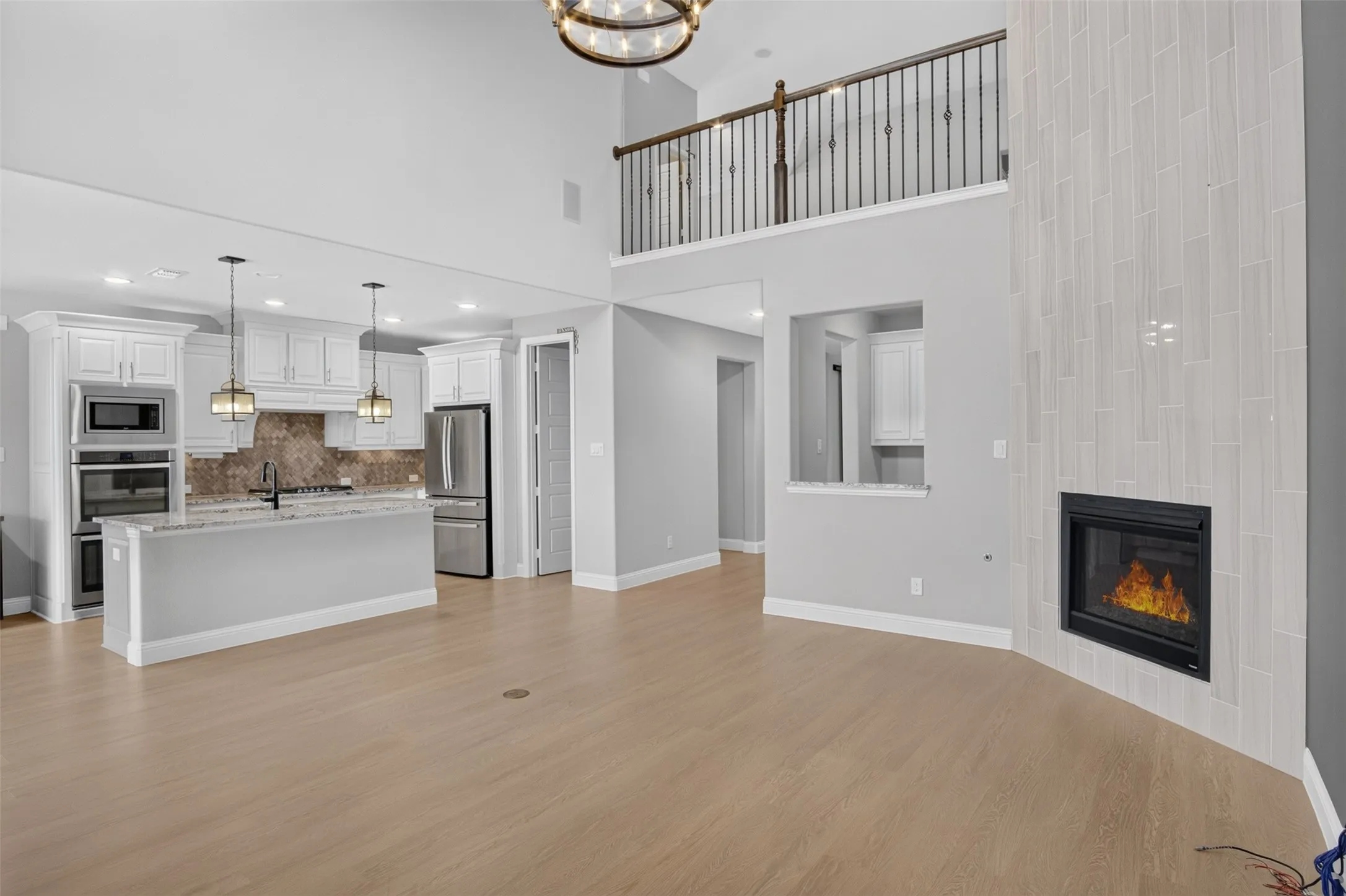 Expansive living space featuring a floor-to-ceiling tiled fireplace, two-story ceiling, and wood-finish flooring