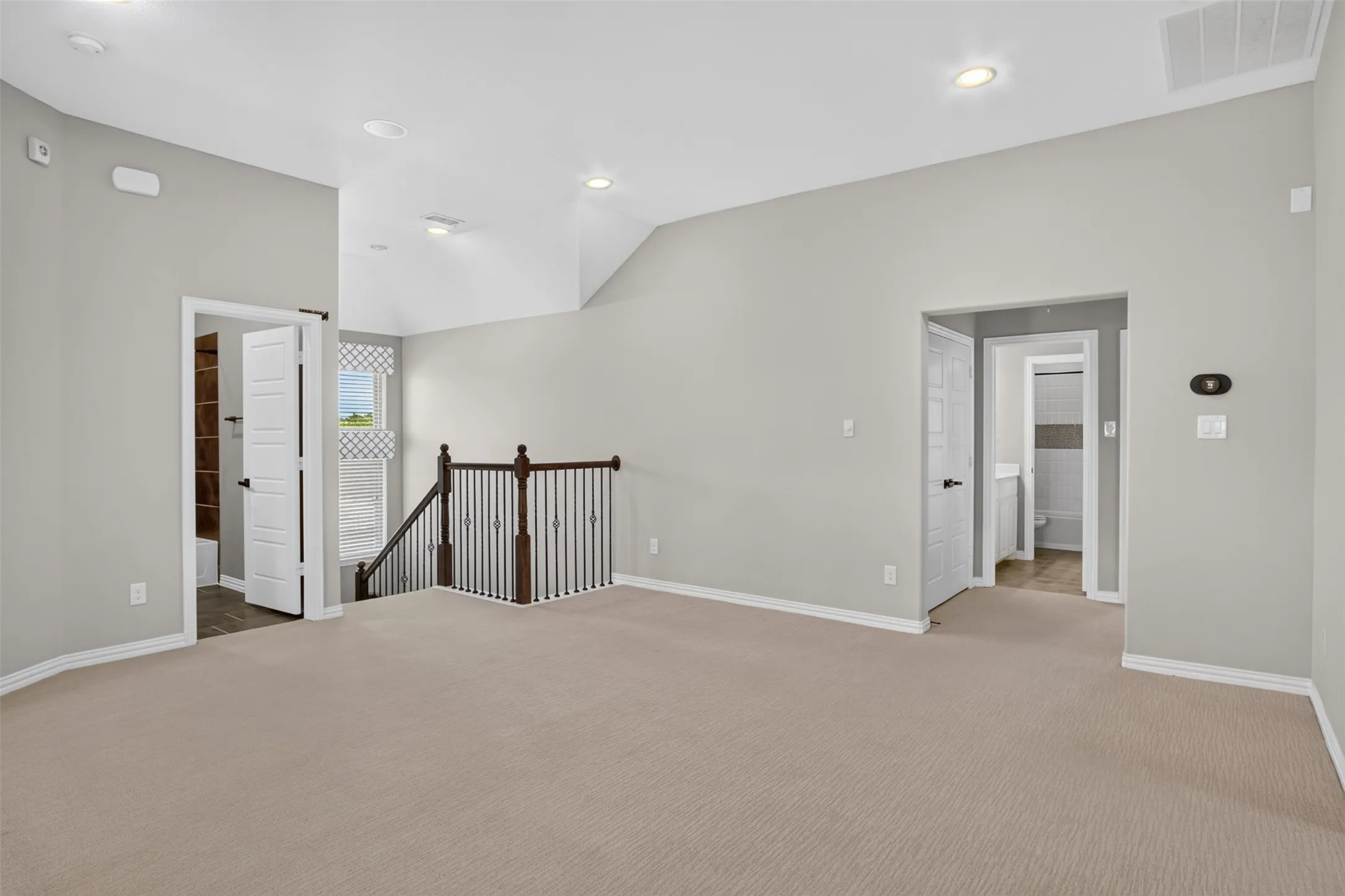 Carpeted landing area featuring vaulted ceilings with recessed lighting, an open stairway with a wood handrail and wrought iron balusters, and two doorways leading to additional rooms