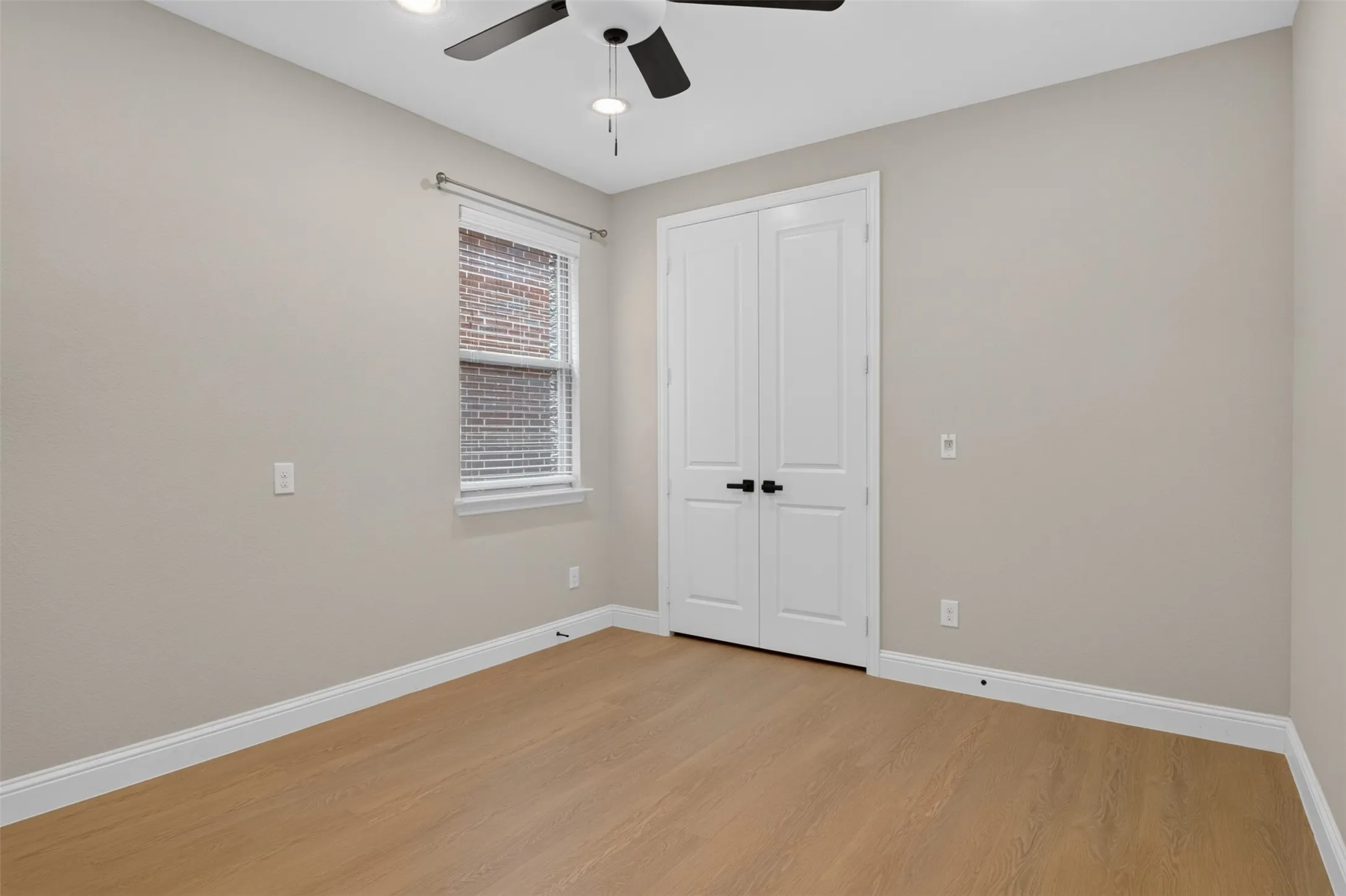 Spacious interior room featuring light wood-finish flooring, neutral painted walls, and white baseboards