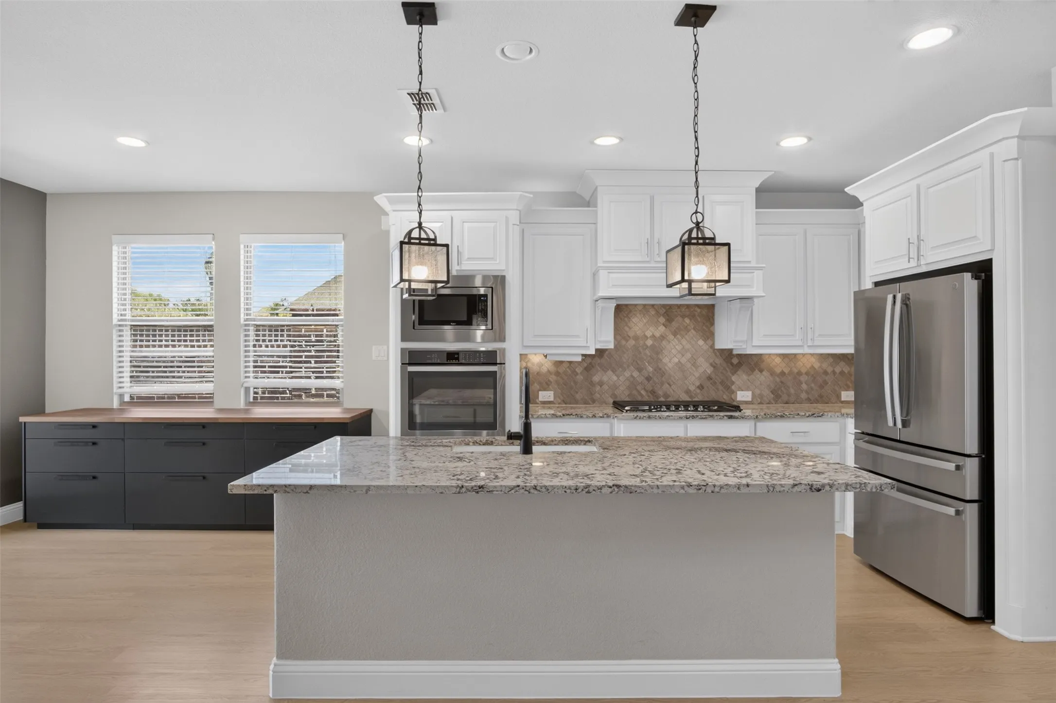 Spacious kitchen featuring an oversized island with granite countertop, white shaker cabinetry, stainless steel appliances, and a mosaic tile backsplash