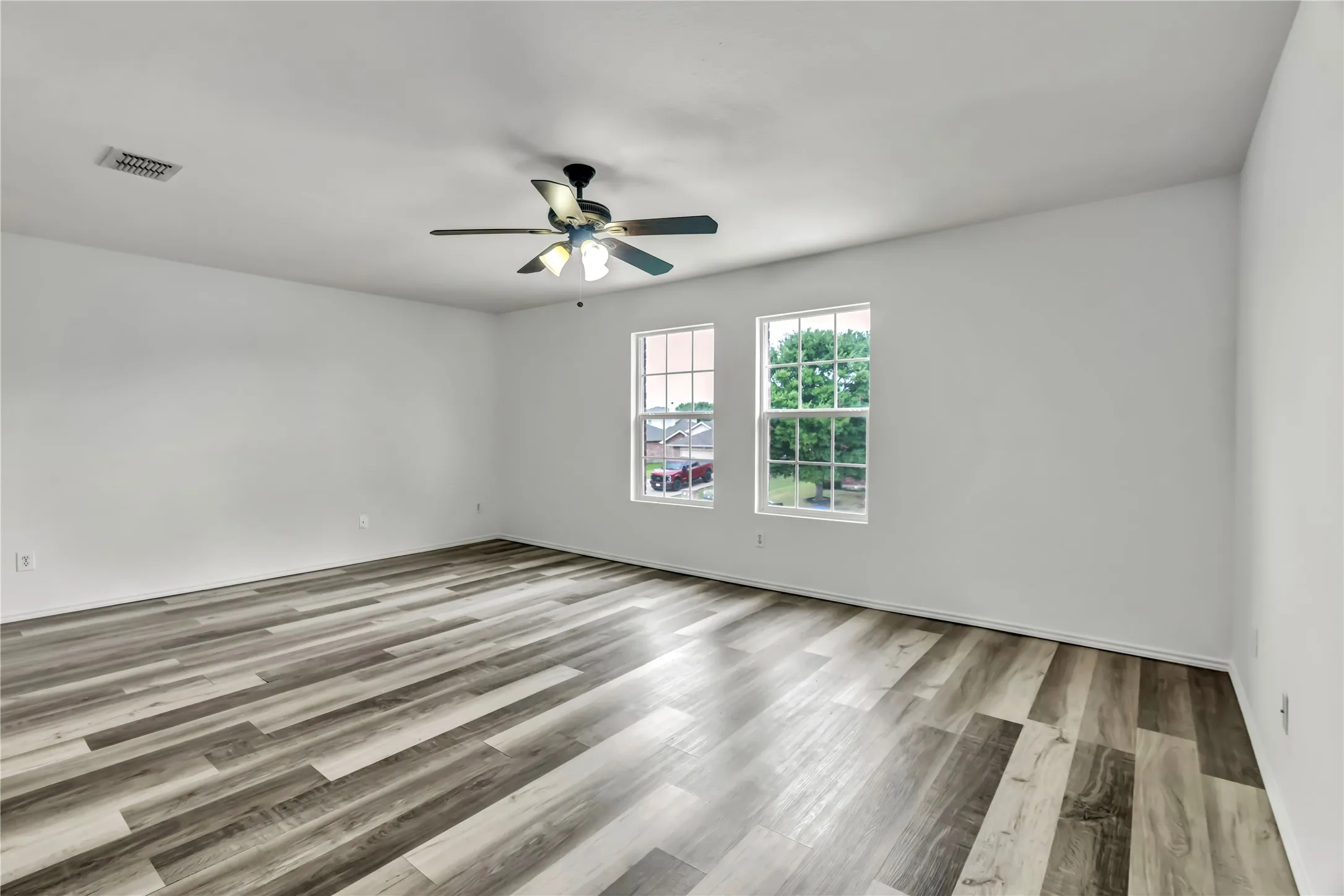 Spacious interior room featuring wood-finish flooring, white walls, and a ceiling fan with integrated lighting