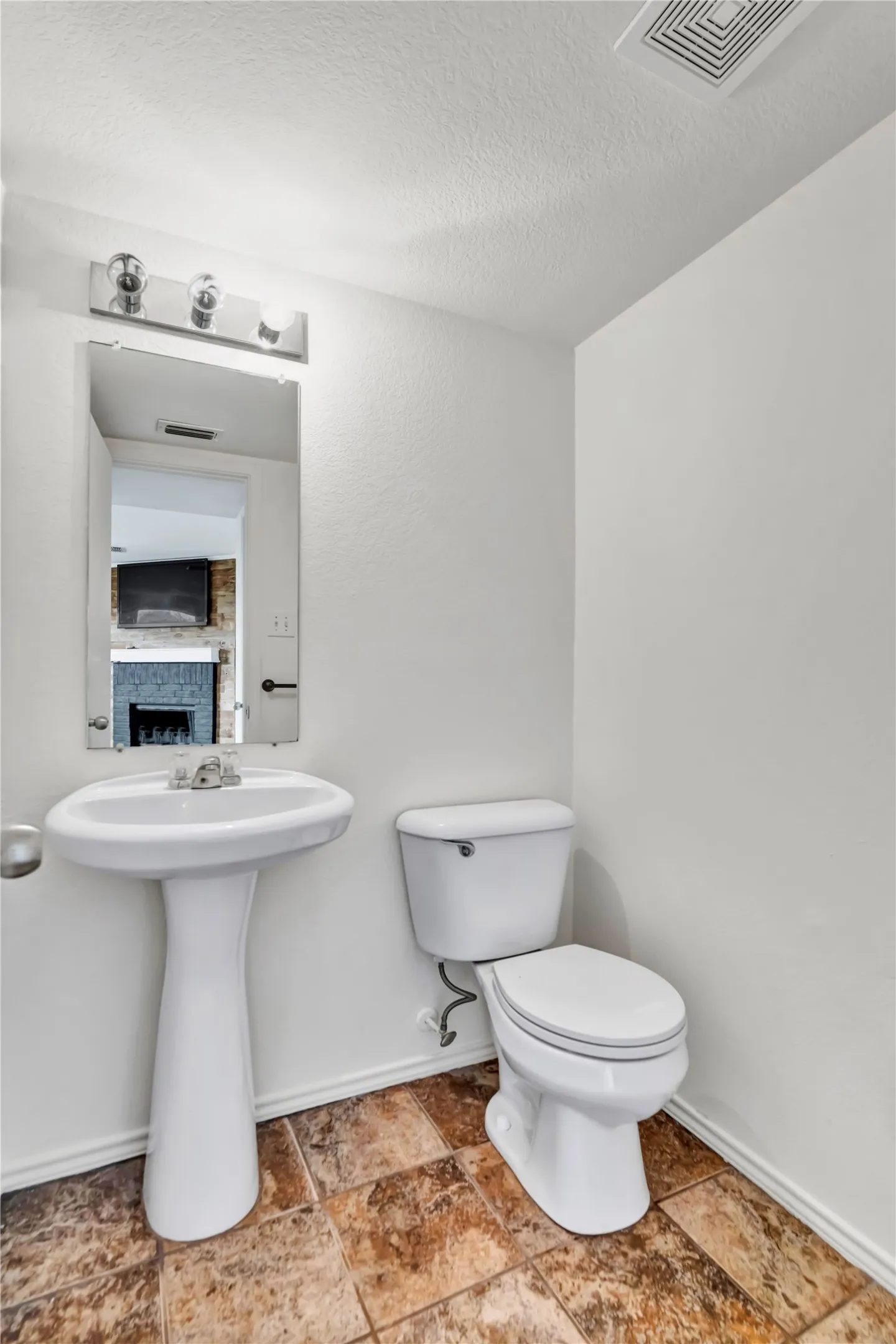 White pedestal sink with a chrome faucet, toilet, and vanity light fixture
