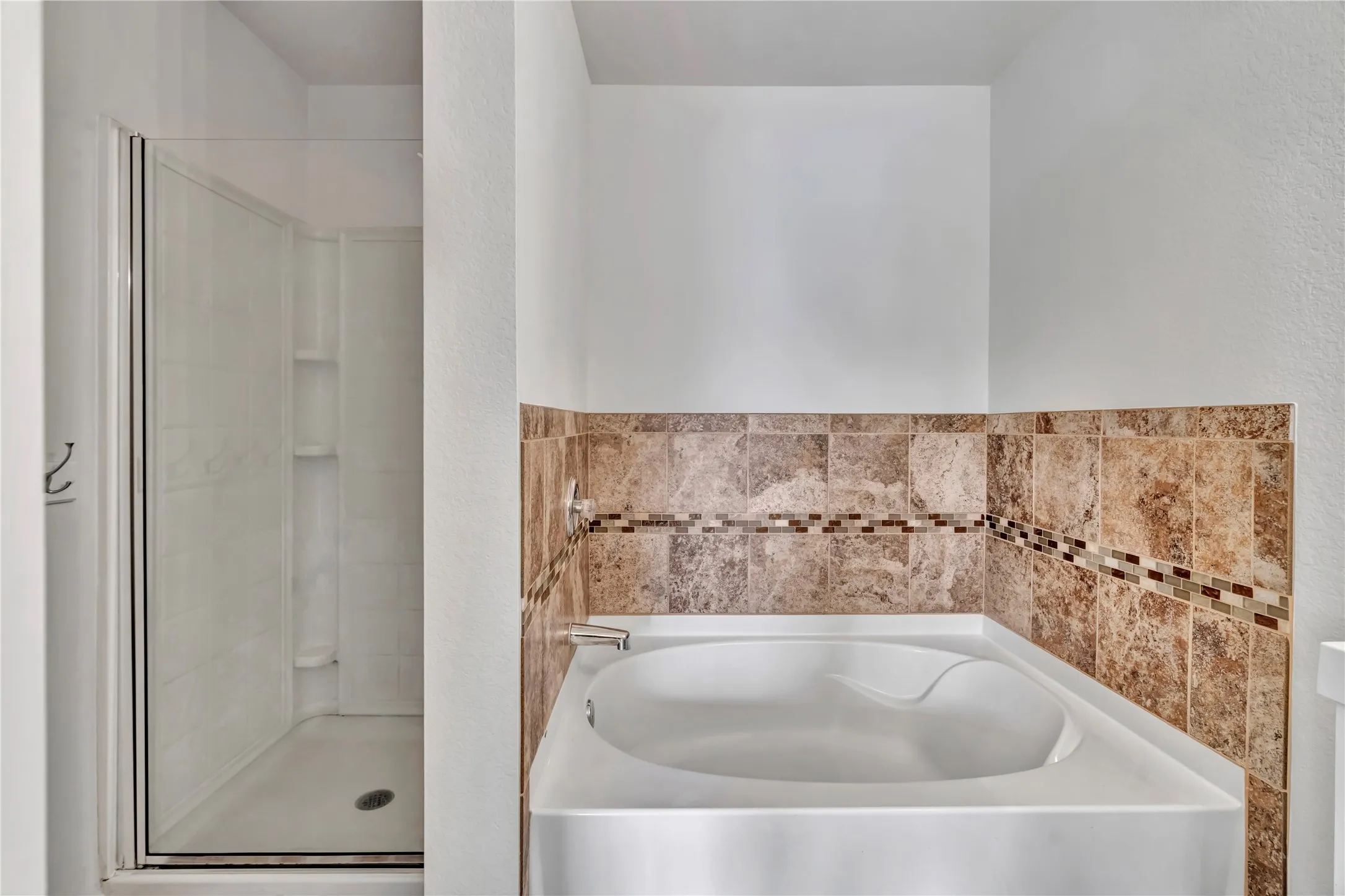 Soaking tub with a tiled surround featuring a decorative mosaic accent band