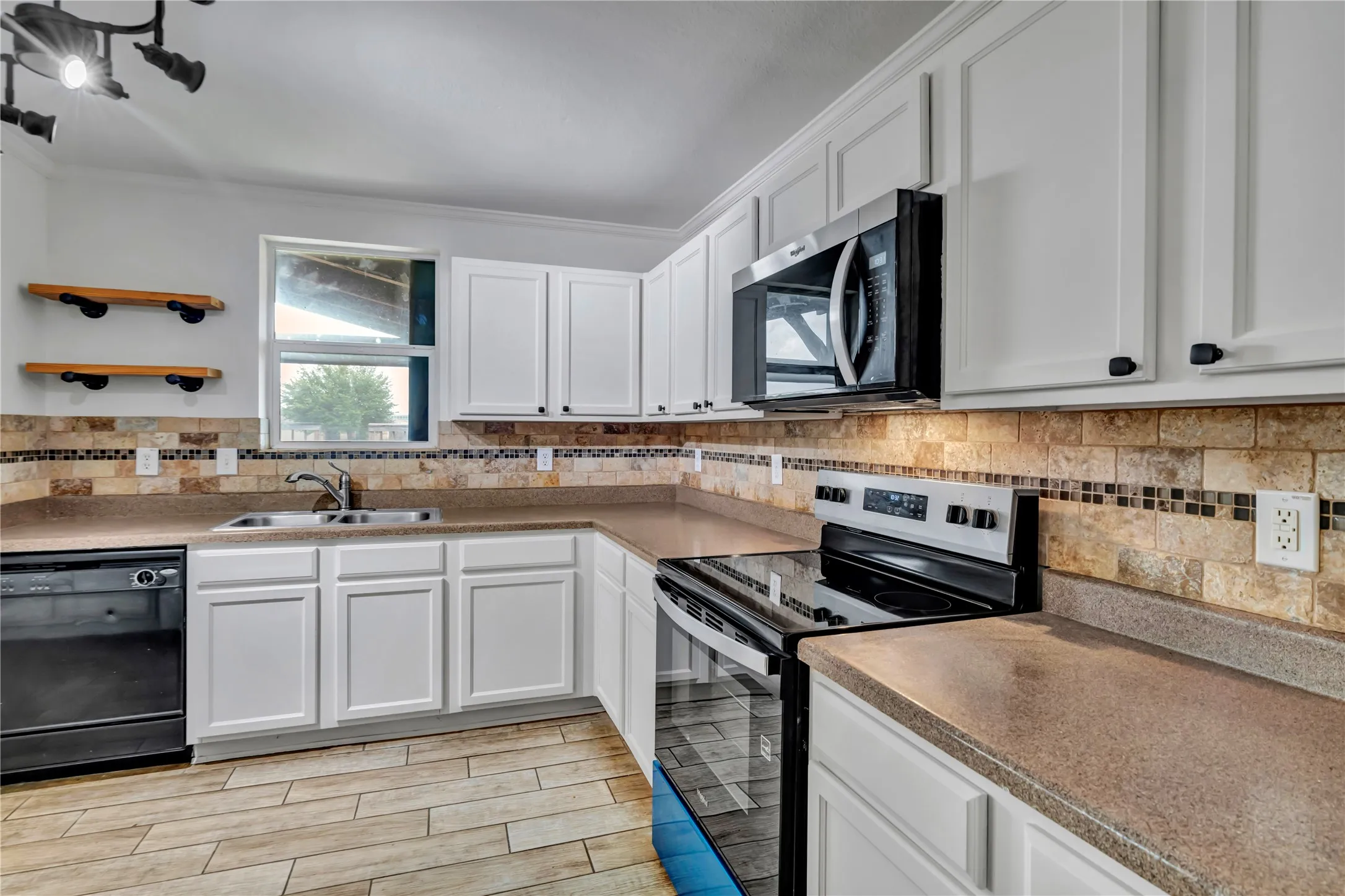 Kitchen featuring white cabinetry, stone-look countertops, a tile backsplash with mosaic accents, stainless steel microwave, and wood-finish flooring