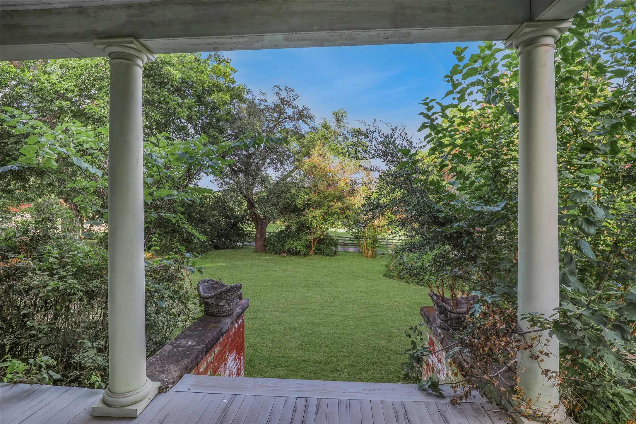 Expansive rear lawn framed by mature trees, visible from a porch featuring classic white columns and a weathered wood-plank floor