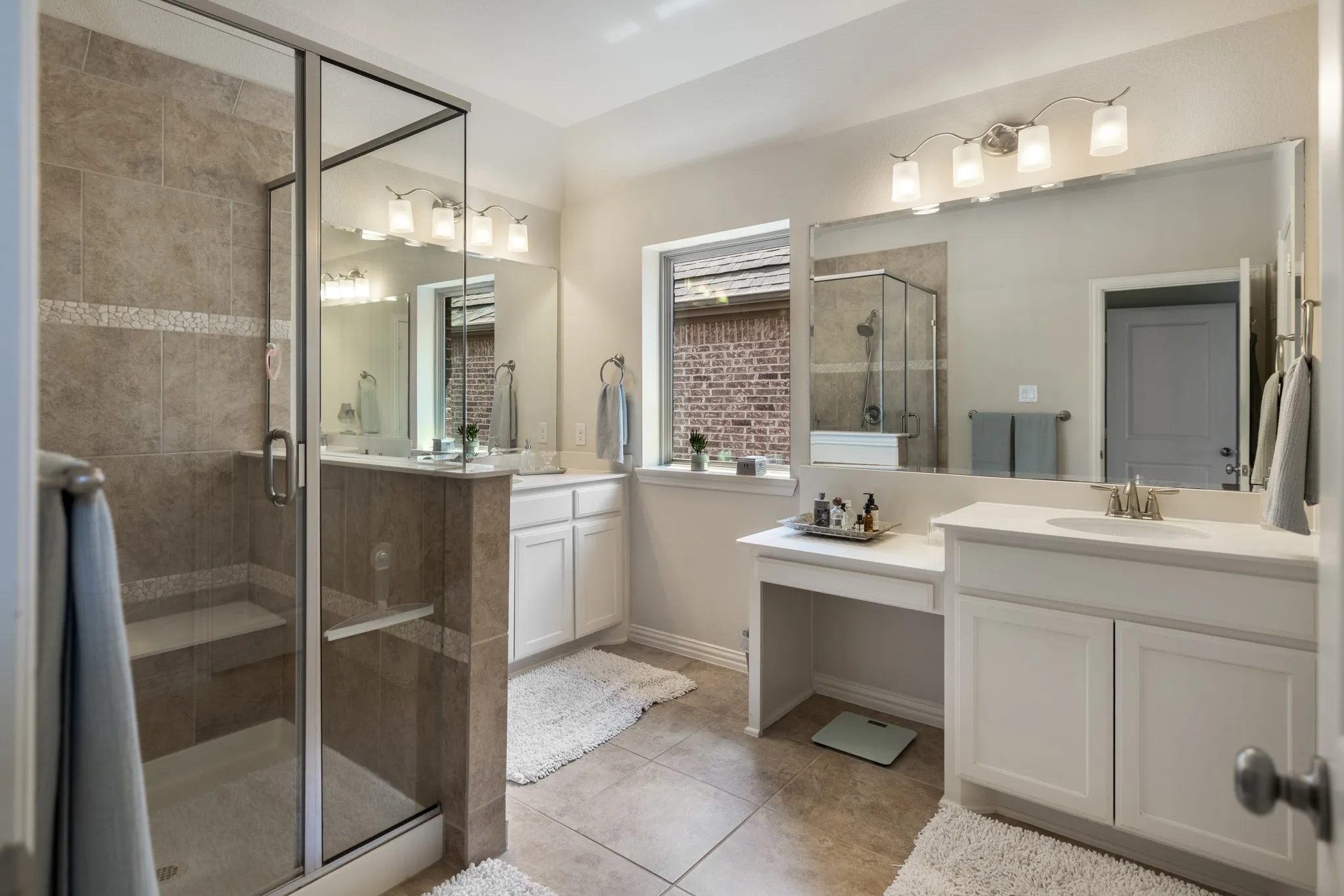 Spacious bathroom featuring a glass-enclosed shower with a built-in bench, dual vanity sinks, white cabinetry, a dedicated vanity space, and large wall-mounted mirrors