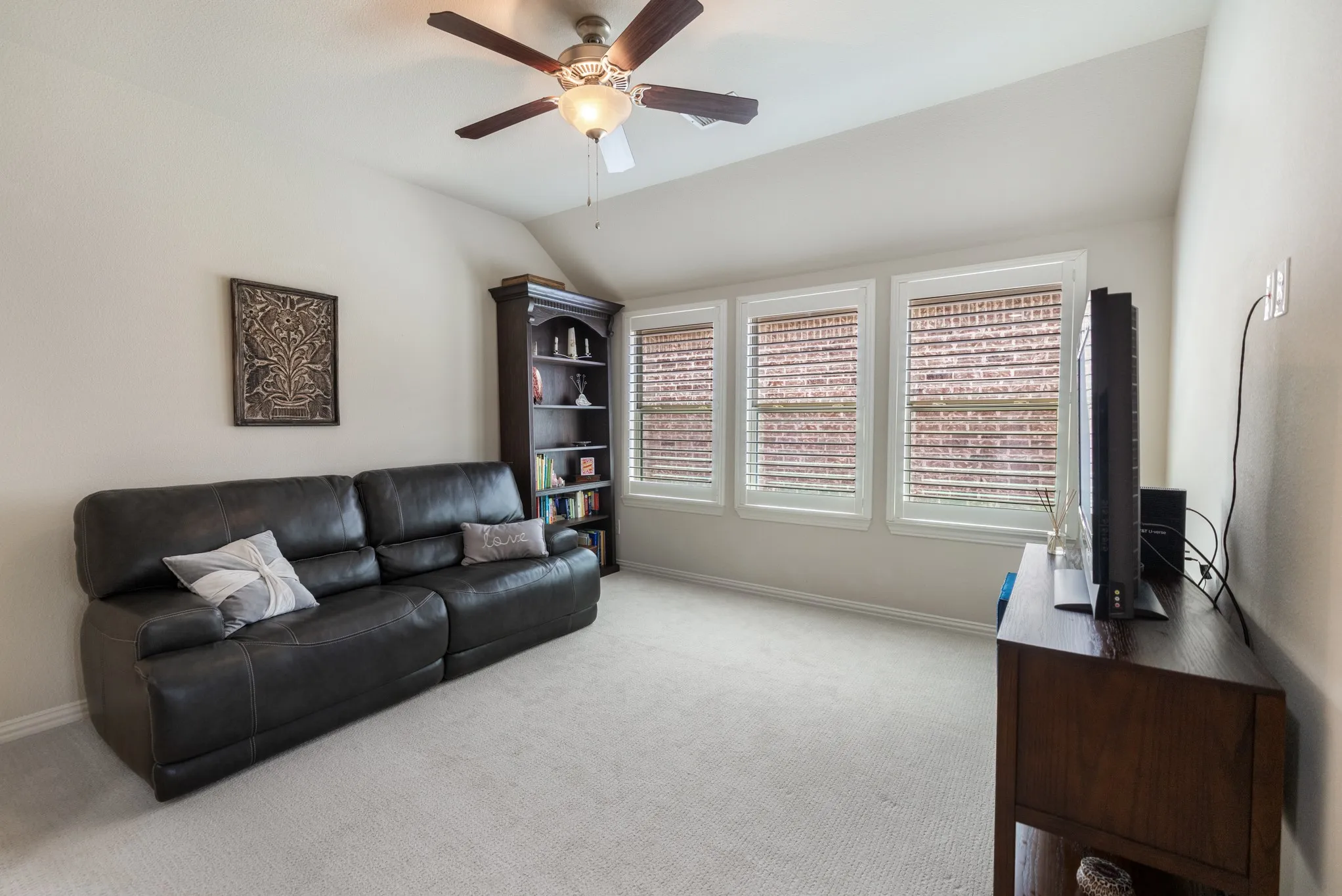 Carpeted room featuring a ceiling fan with light fixture, three windows with blinds, and light-toned walls