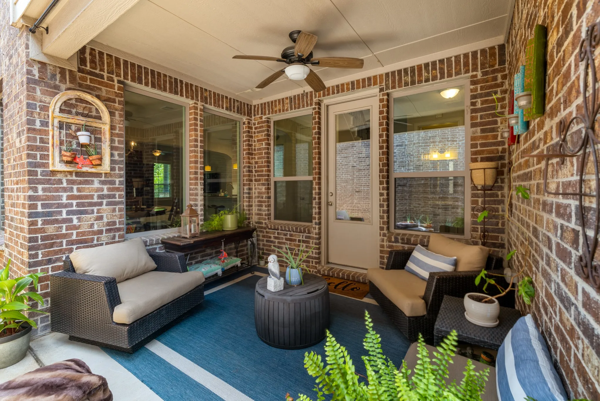 Covered patio featuring brick walls, a ceiling fan, multiple windows, and a glass-paneled door