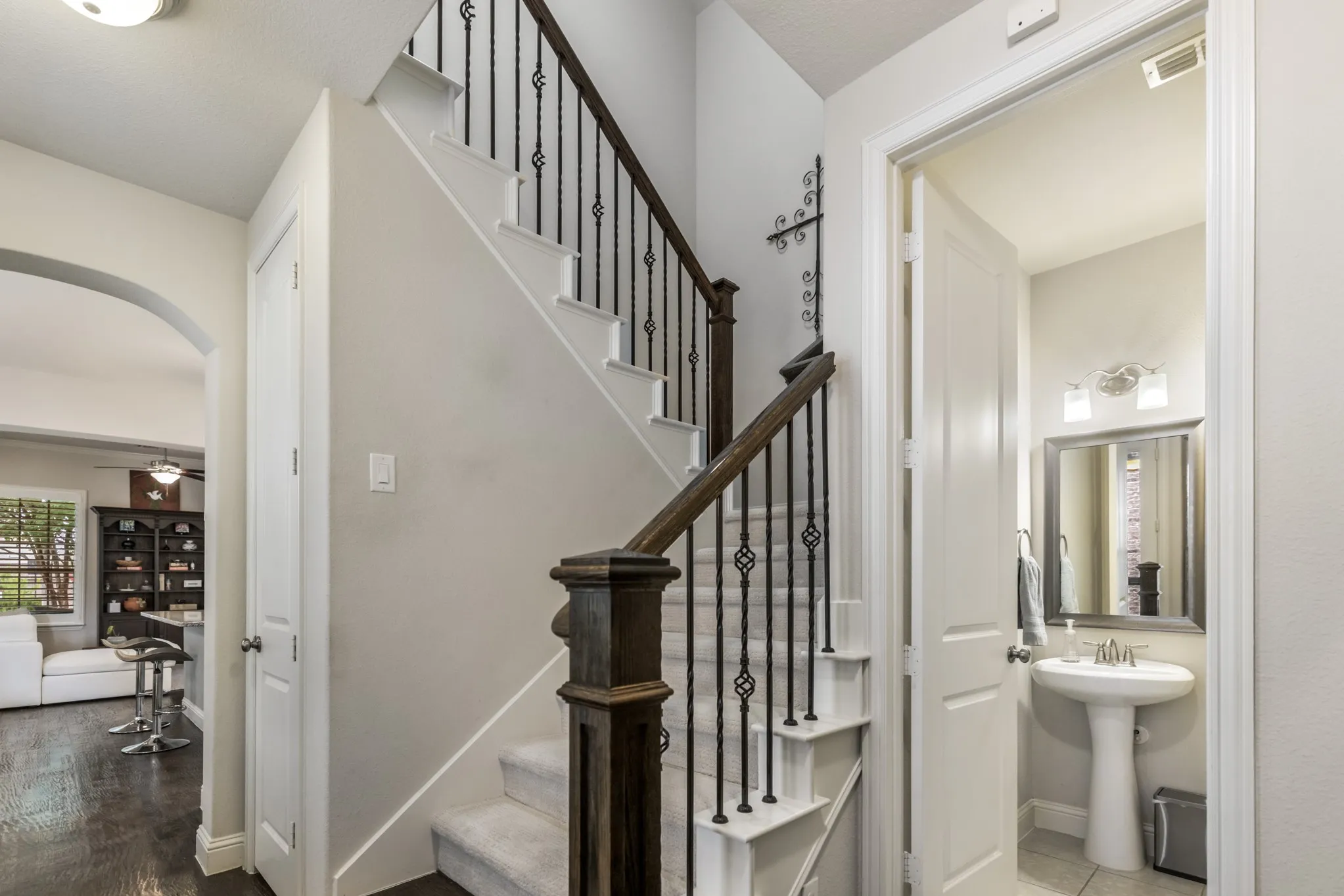 Staircase with wrought iron balusters and dark wood handrail, carpeted treads, and a white riser