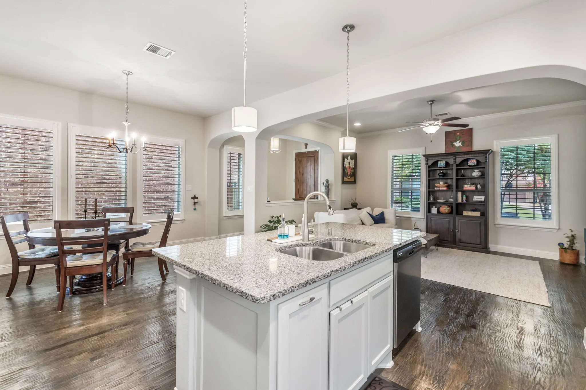 Kitchen island featuring a dual basin sink with a gooseneck faucet, light granite countertop, and white​​‌​​​​‌​​‌‌​‌‌​​​‌‌​‌​‌​‌​​​‌​​ cabinetry