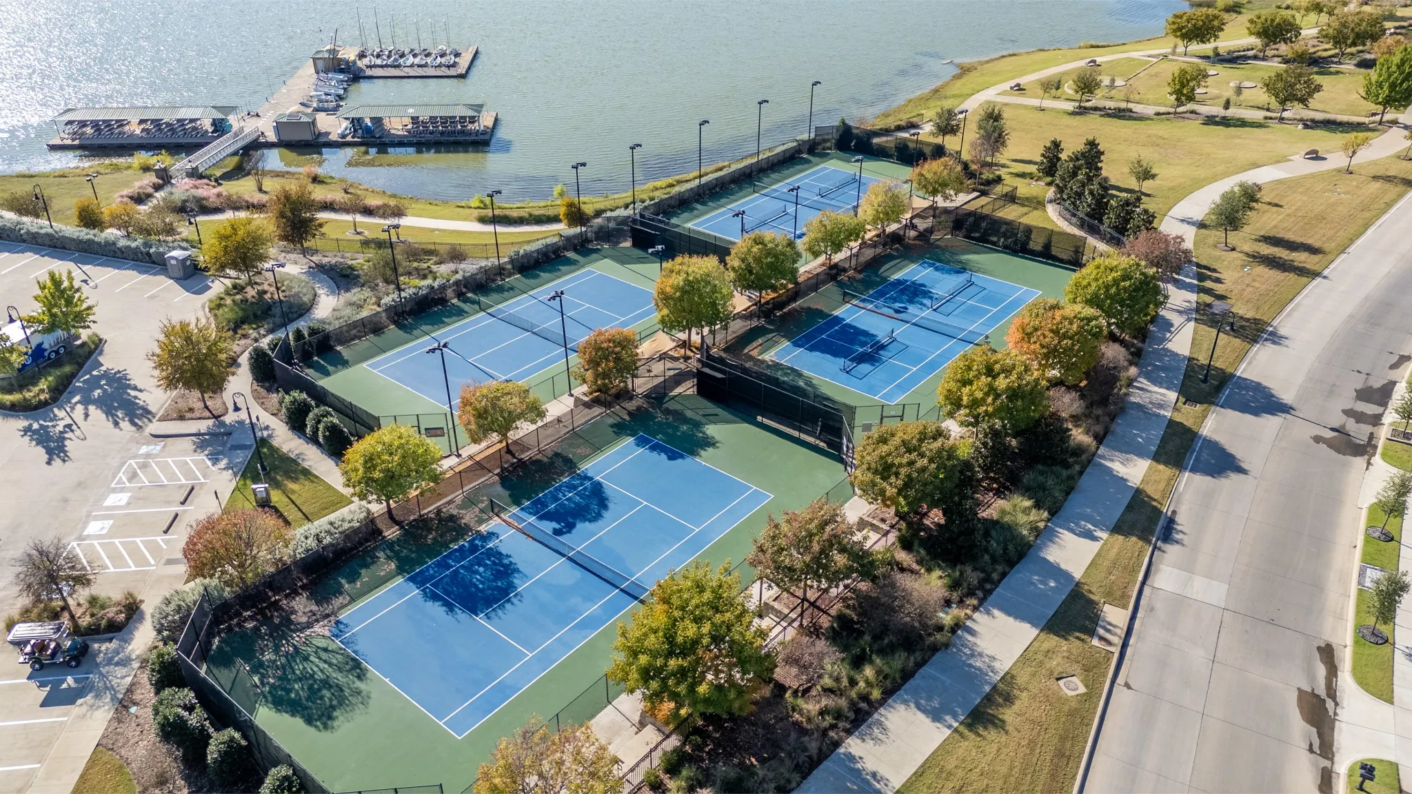 Four outdoor tennis courts featuring blue playing surfaces and green surrounds