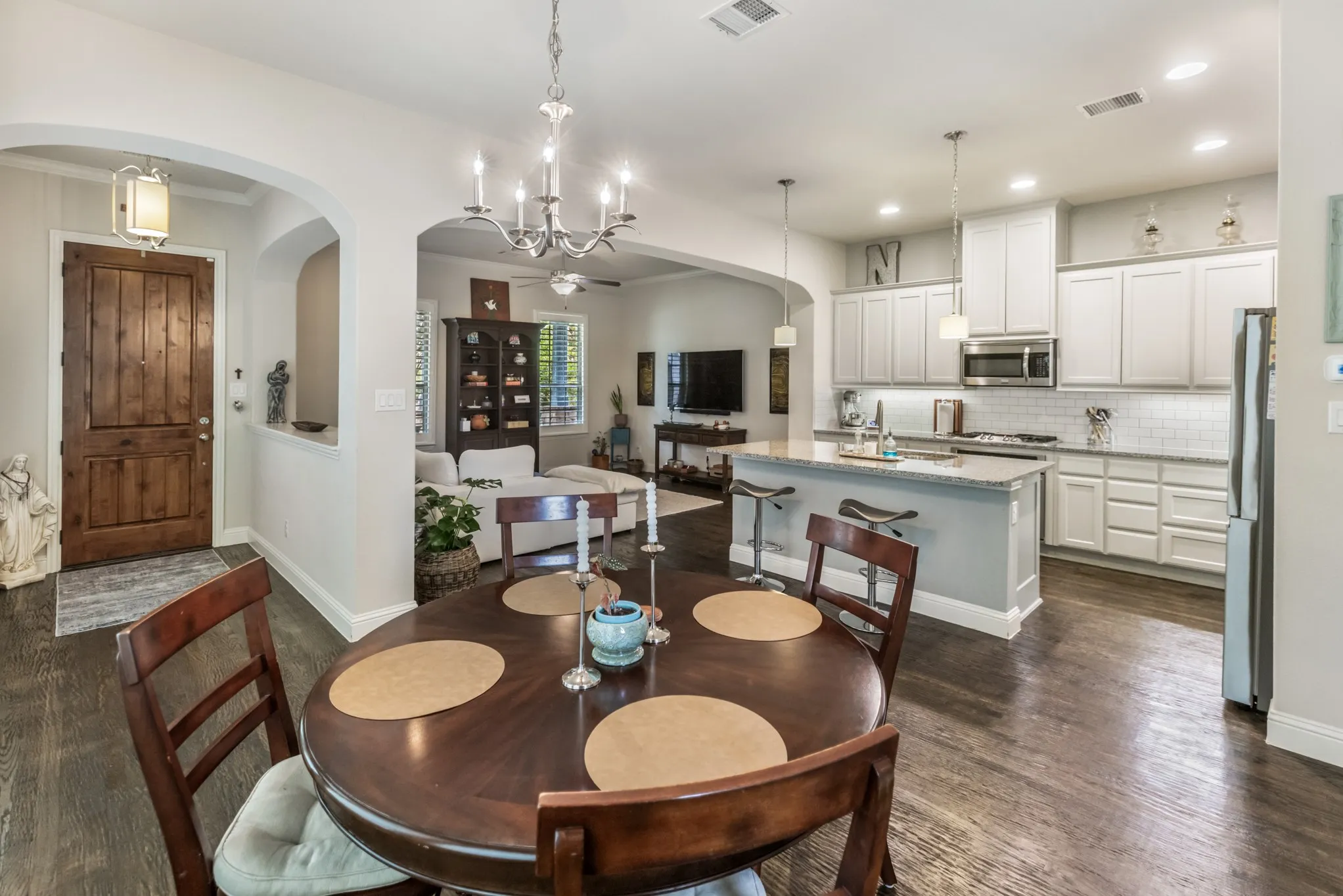 Open-concept living space featuring wood-finish flooring, a kitchen with white cabinetry and stainless-steel appliances, a kitchen island with seating, pendant lighting, and a chandelier in the dining area