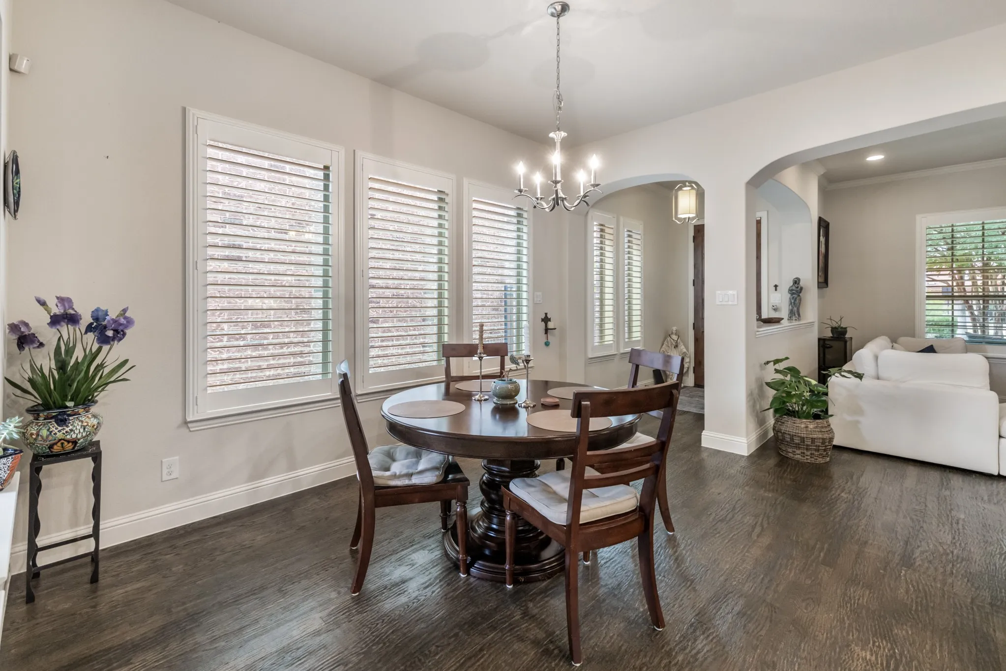 Dining area featuring dark wood-finish flooring, white plantation shutters, and a chrome chandelier