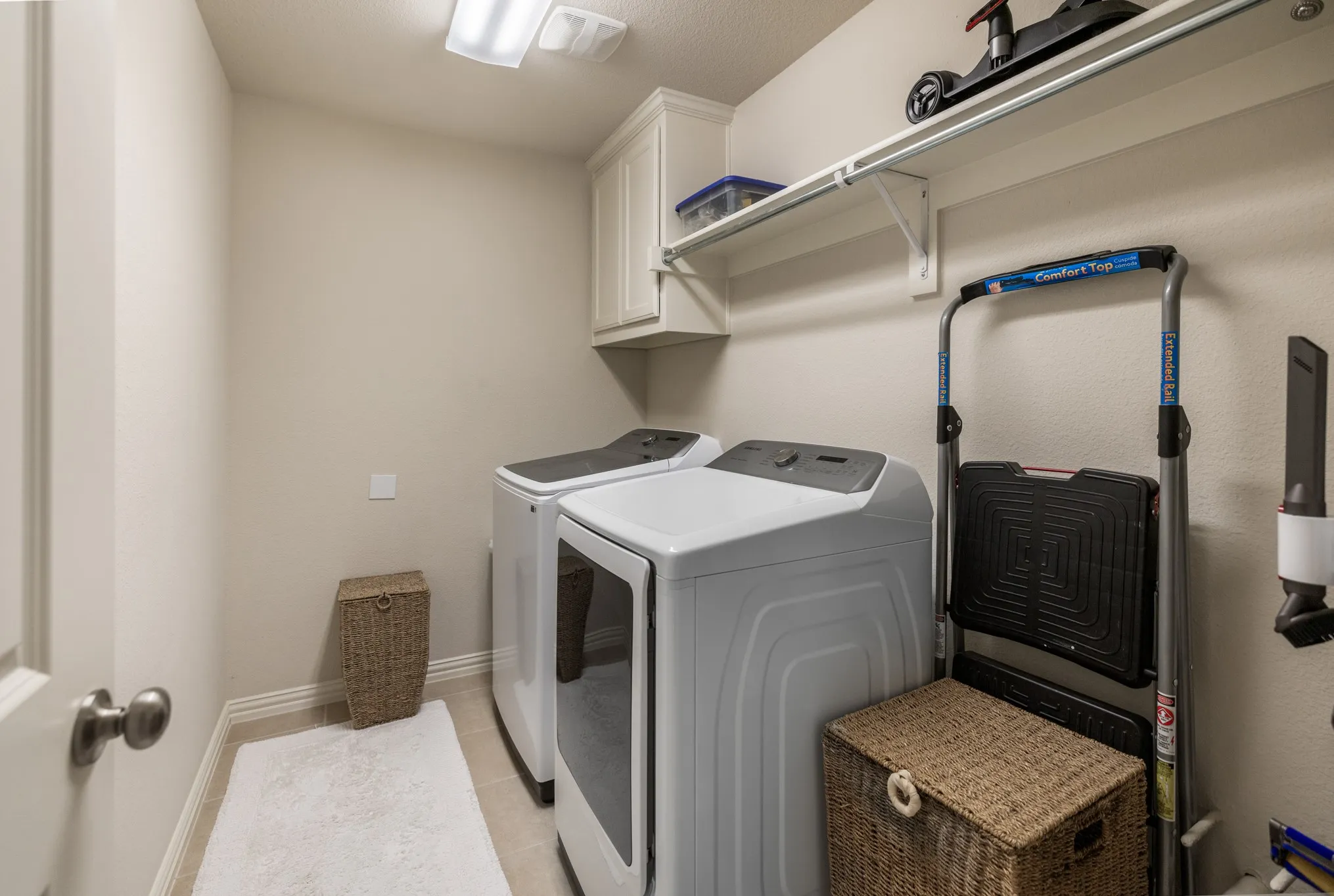 Dedicated laundry area featuring tile flooring, neutral wall tones, upper cabinetry, and integrated shelving