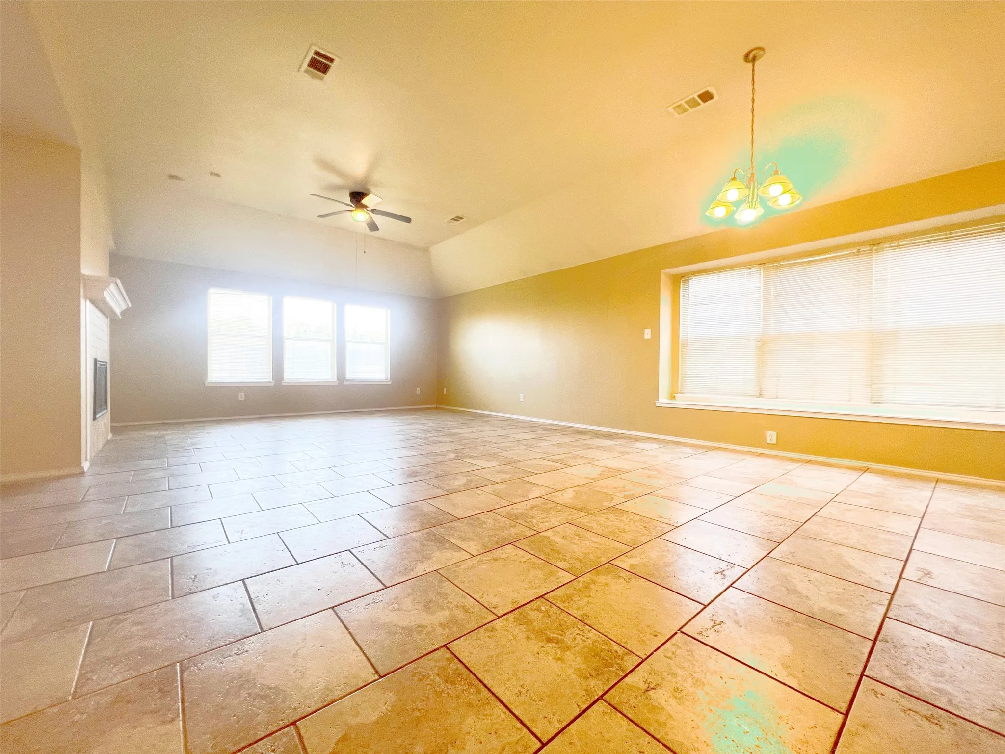 Spacious room featuring vaulted ceilings, a fireplace with a white mantel, an overhead ceiling fan, and large tile flooring