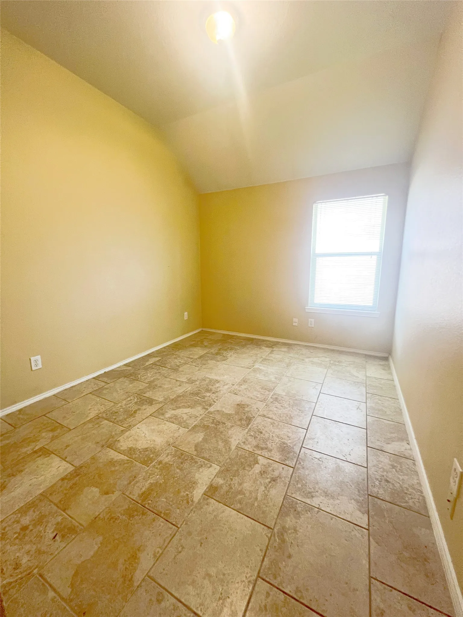Room featuring large format floor tiling, a single window with blinds, and light-toned walls