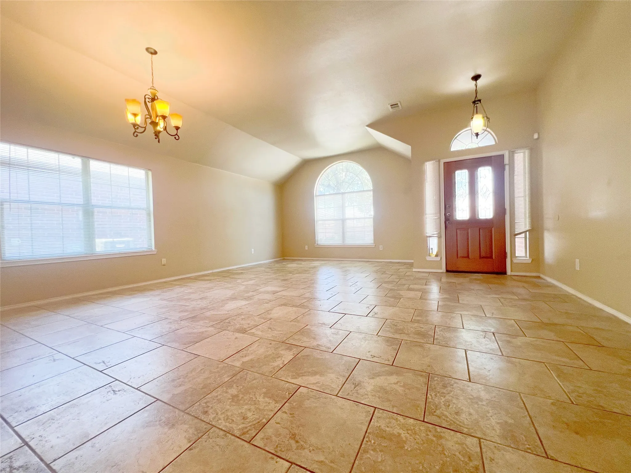 Spacious interior featuring large format tile flooring, vaulted ceilings, and a prominent front entry door with transom window