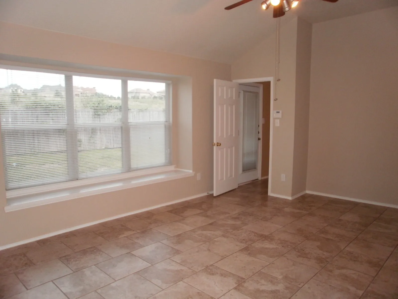 Spacious room featuring vaulted ceilings, light-toned tile flooring, and a large window with an integrated window seat