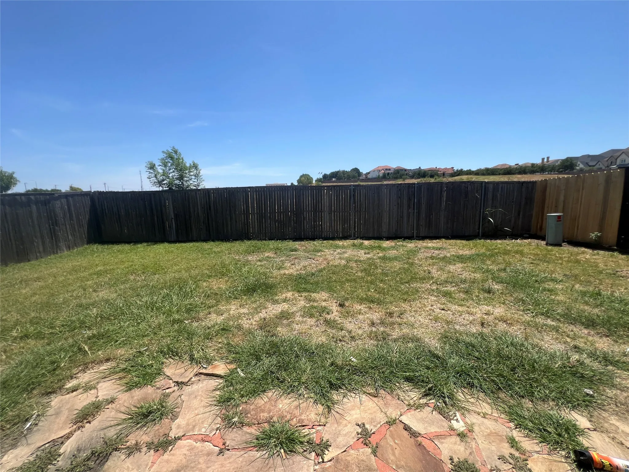 Fenced backyard featuring flagstone patio, expansive grass area, and mature perimeter fencing