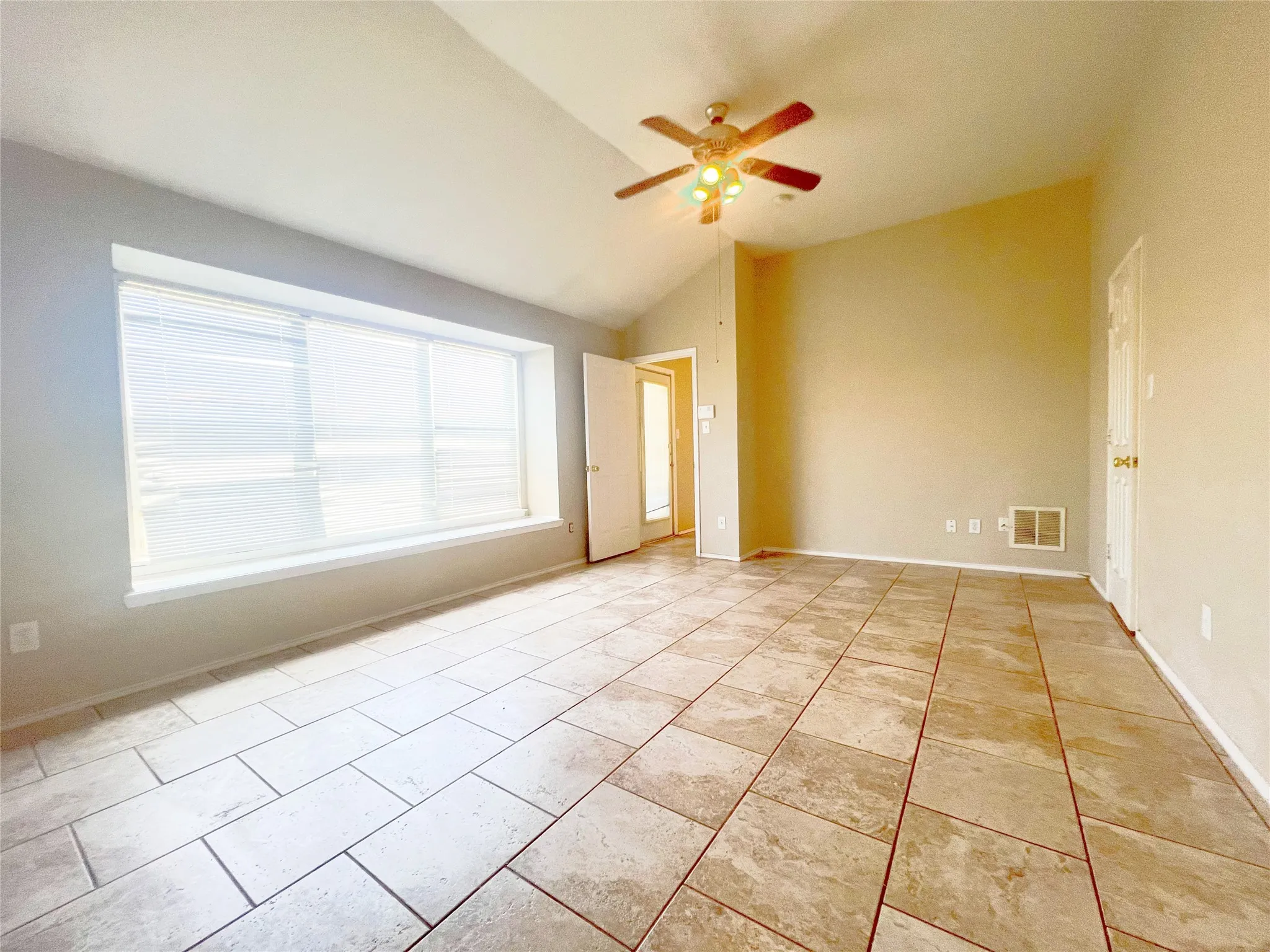 Spacious room featuring large format tile flooring, a vaulted ceiling, and a ceiling fan with integrated lighting