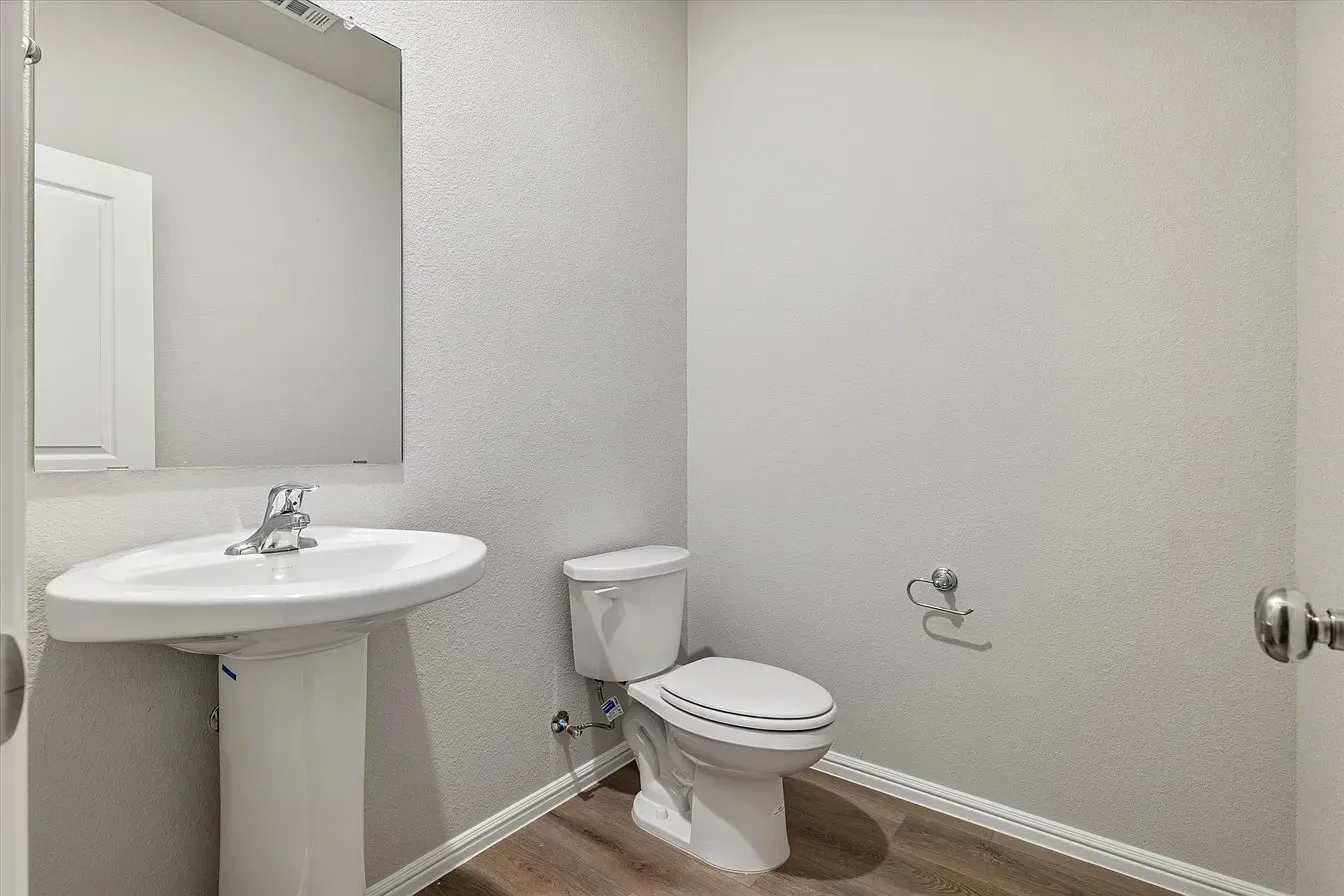 Bathroom featuring a pedestal sink with a chrome faucet, wall-mounted mirror, and wood-finish flooring