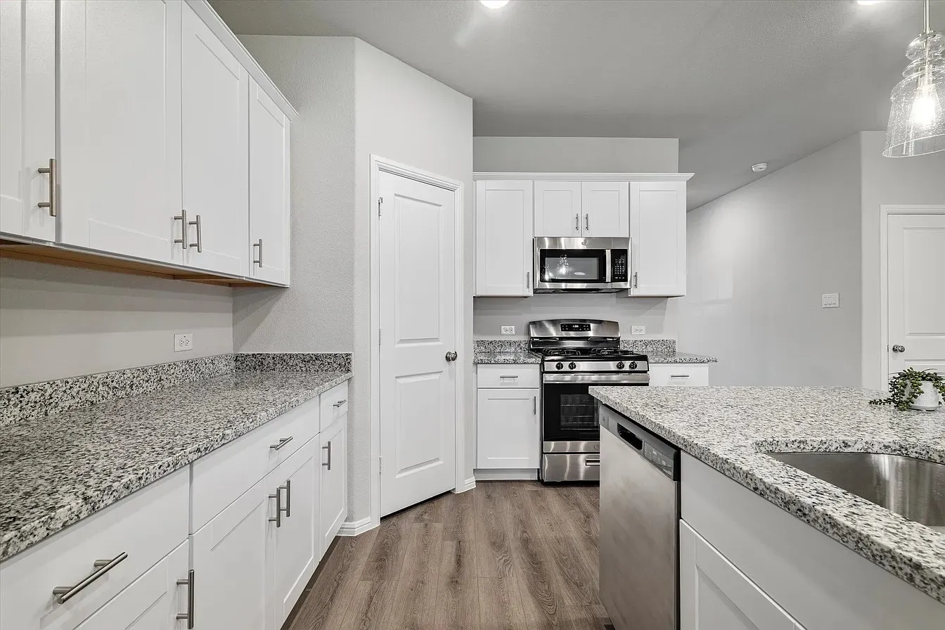 Spacious kitchen featuring white cabinetry, granite countertops, wood-finish flooring, stainless steel appliances, and an island with an undermount sink