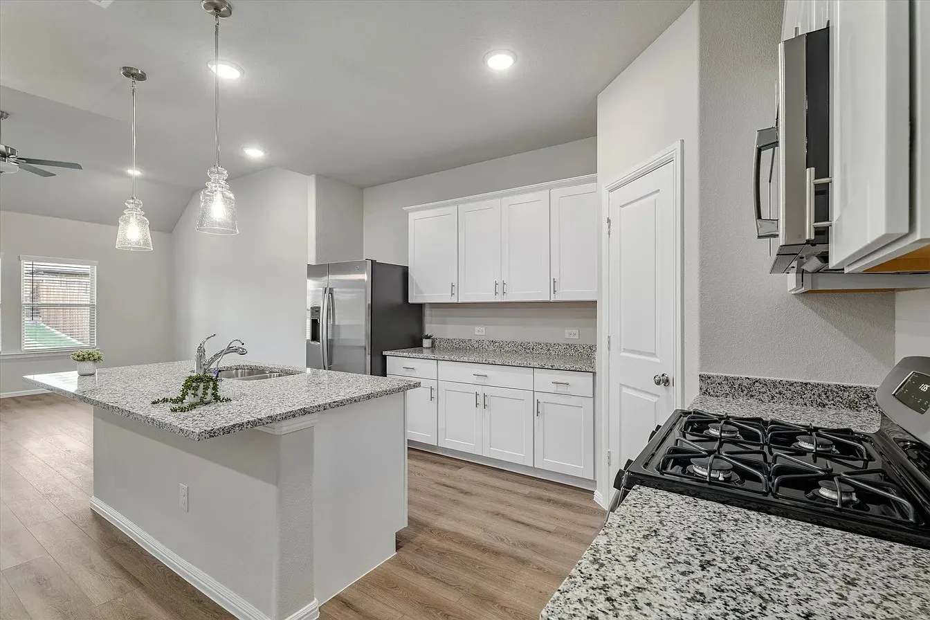 Kitchen featuring an island with an integrated sink, granite countertops, white cabinetry, and wood-finish flooring