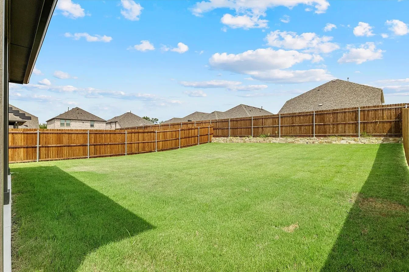 Expansive green lawn enclosed by a tall wood privacy fence with a stone base