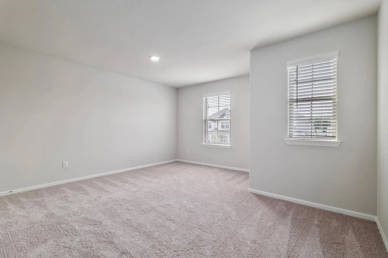 Spacious room featuring neutral carpeting, light gray wall paint, and two windows with white blinds