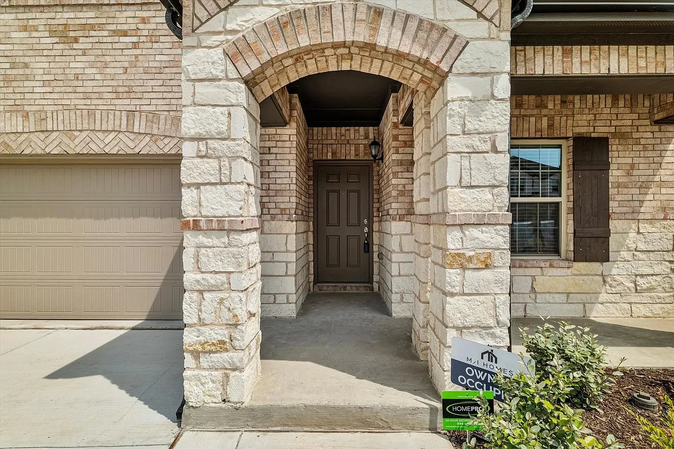 Stone and brick exterior with an arched entryway, a paneled front door, a multi-pane window with dark shutters, and a two-car garage with a panel door