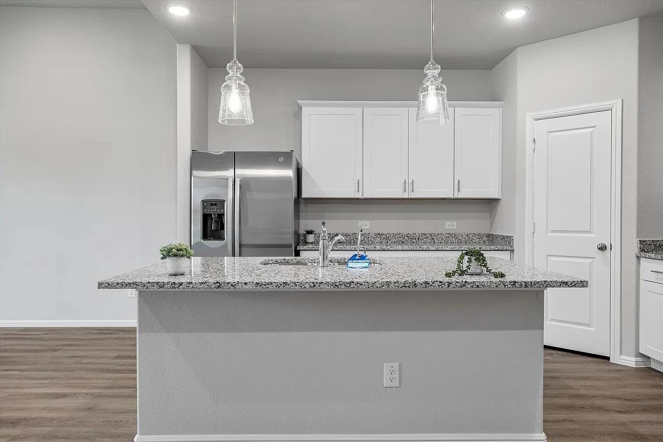 Kitchen island featuring granite countertops, a stainless steel sink with a chrome faucet, and two decorative pendant lights