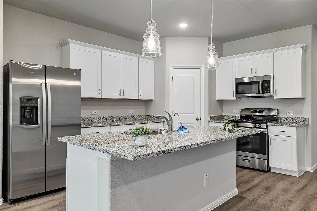 Modern kitchen featuring white shaker cabinetry, stainless steel appliances, speckled granite countertops, a center island with a sink, and wood-finish flooring